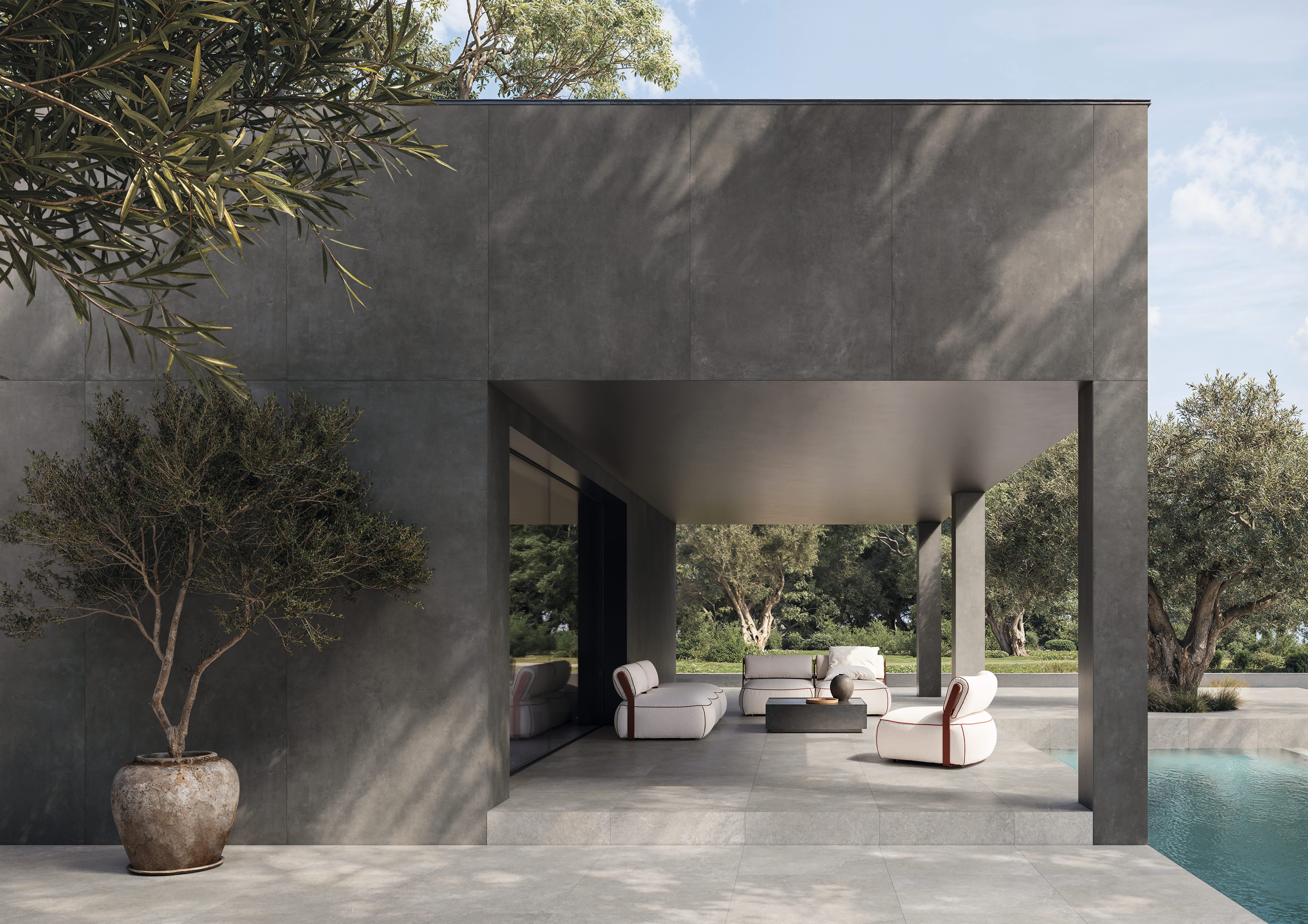 Concrete porcelain tile in Dark cladding a poolside pavilion, with light stone paving, olive trees and lounge seating
