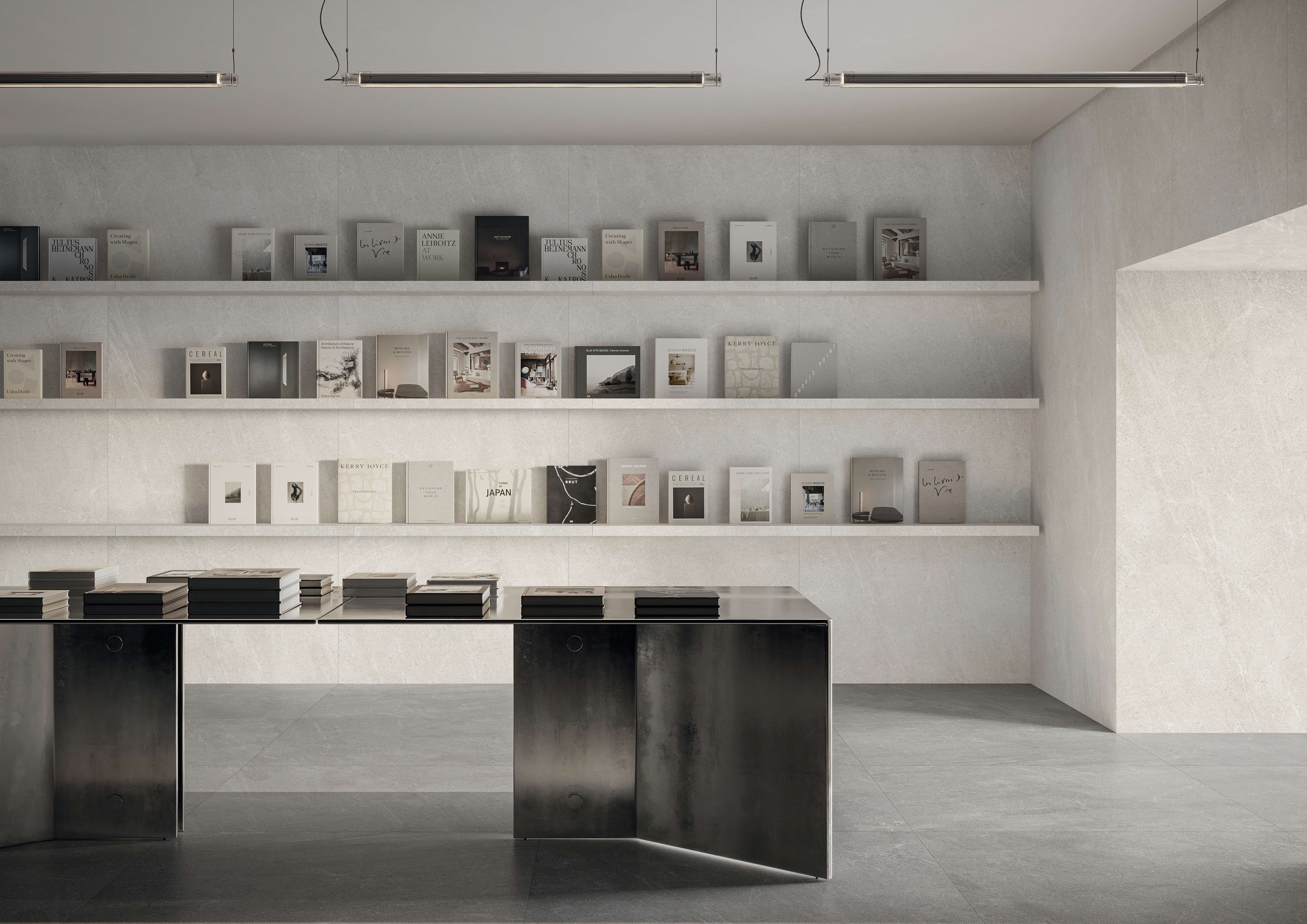Bookshop interior in soft grey Mega Natural porcelain, with wall shelving of books and a dark metal display desk.