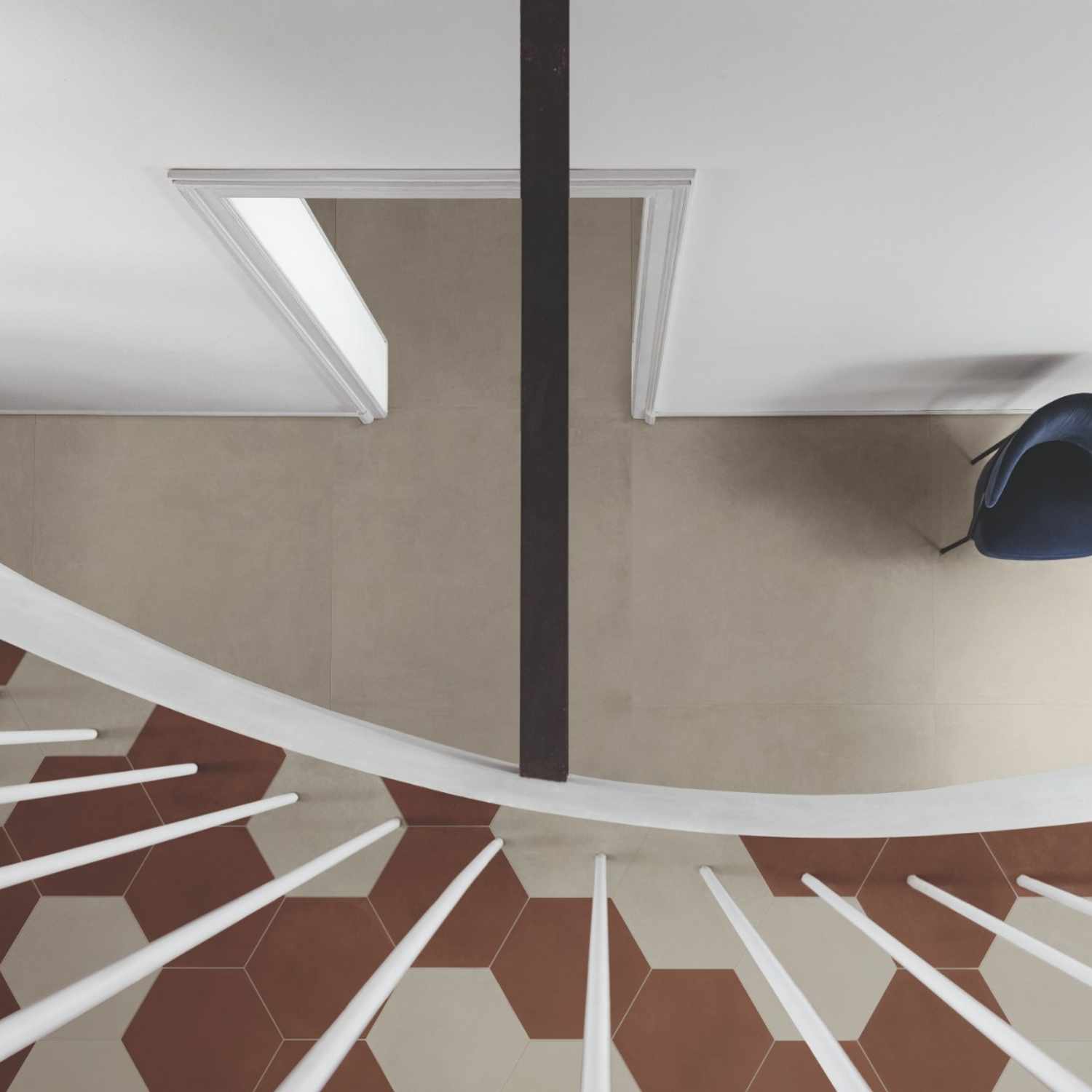 Cementum cement-look porcelain tile installed as wall cladding in a modern staircase area with overhead view showing white spiral stairs and hexagonal floor tiles