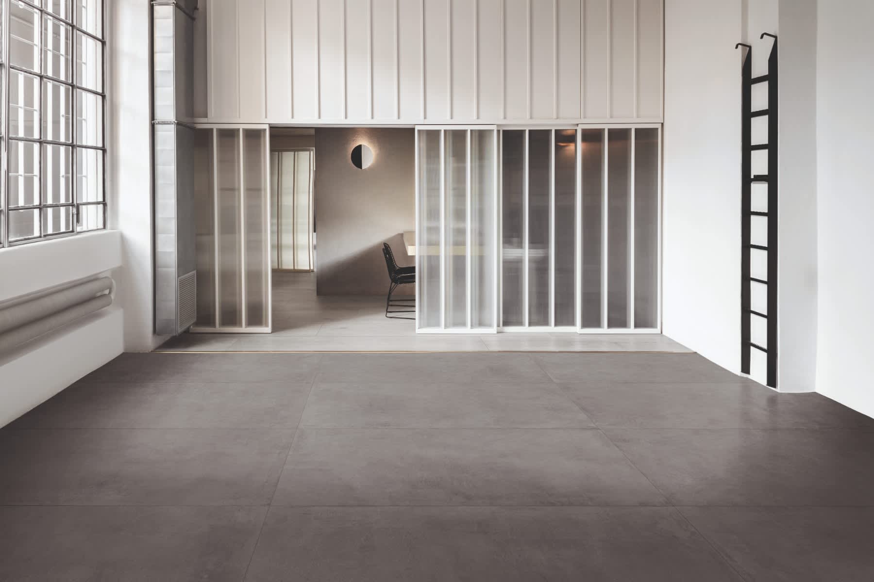 Cementum cement-look porcelain tile in dark gray installed as flooring in a modern loft space with industrial windows and white partitions