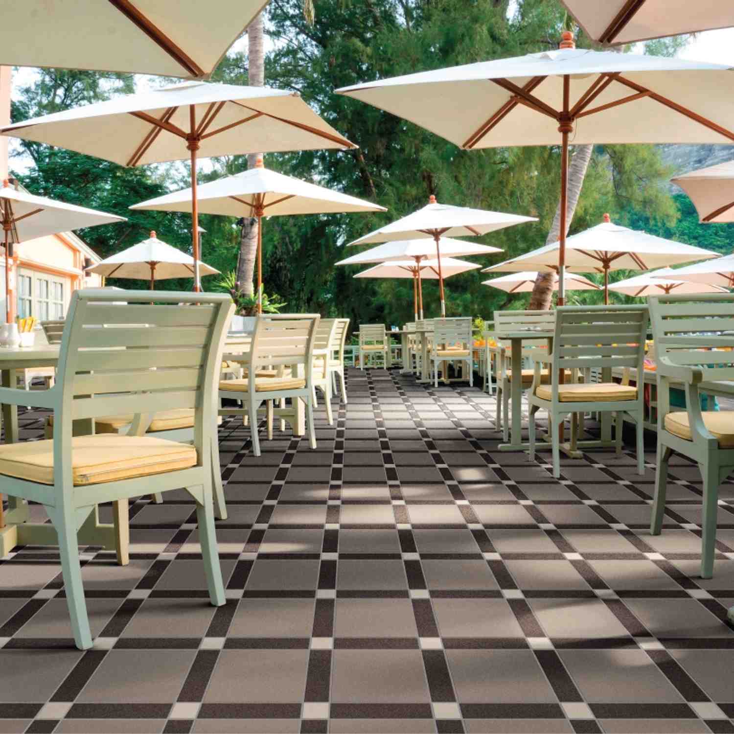 Cesi glazed porcelain stoneware floor tiles in black and white diamond checkerboard pattern on outdoor restaurant patio with white wooden chairs cream cushions parasol umbrellas and tropical greenery