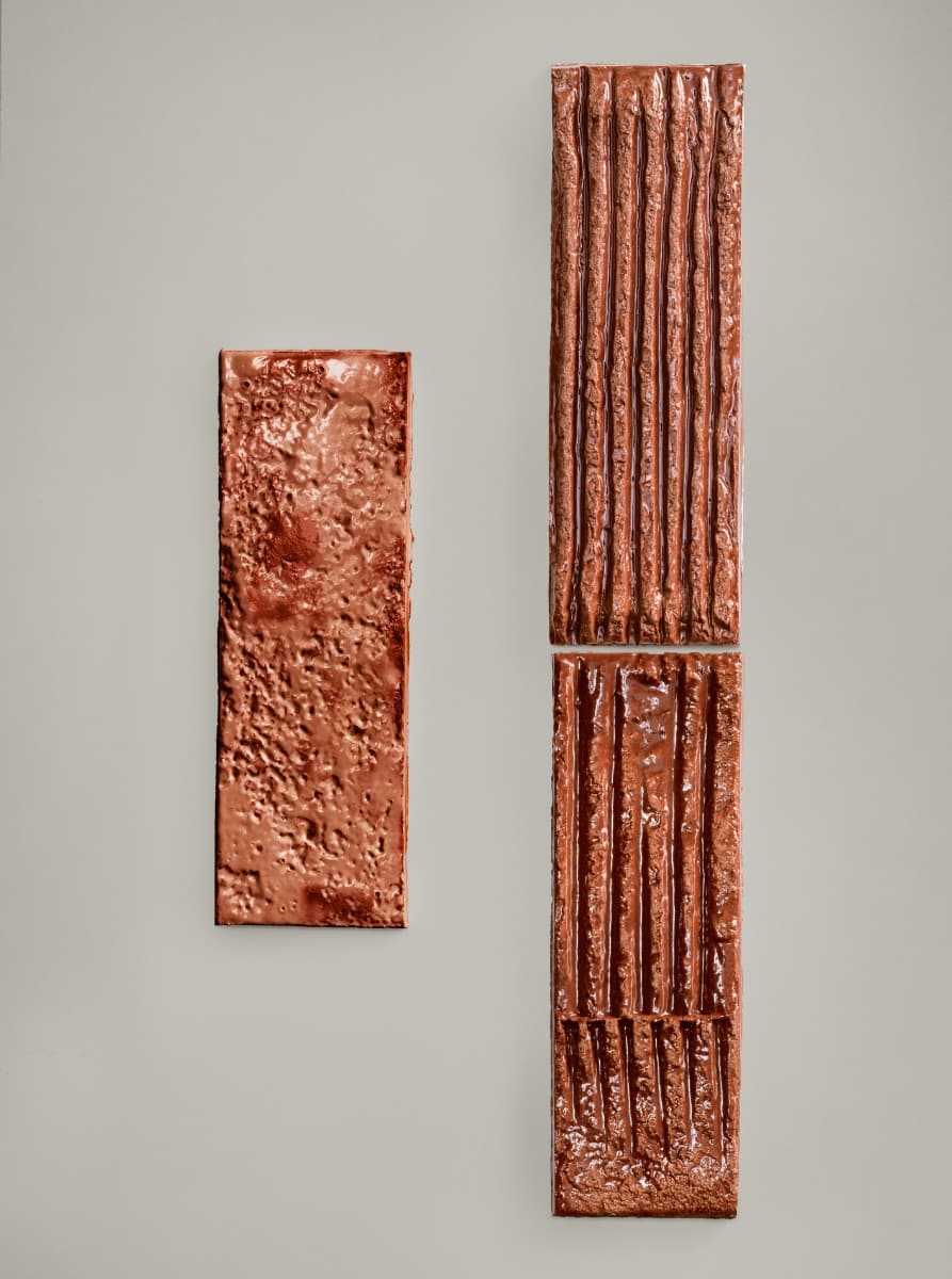 Mutina Chamotte Terra high-gloss glazed ceramic wall tile samples standing upright showing Mono smooth and Linea grooved pattern variations in warm copper brown with artistic glaze finish