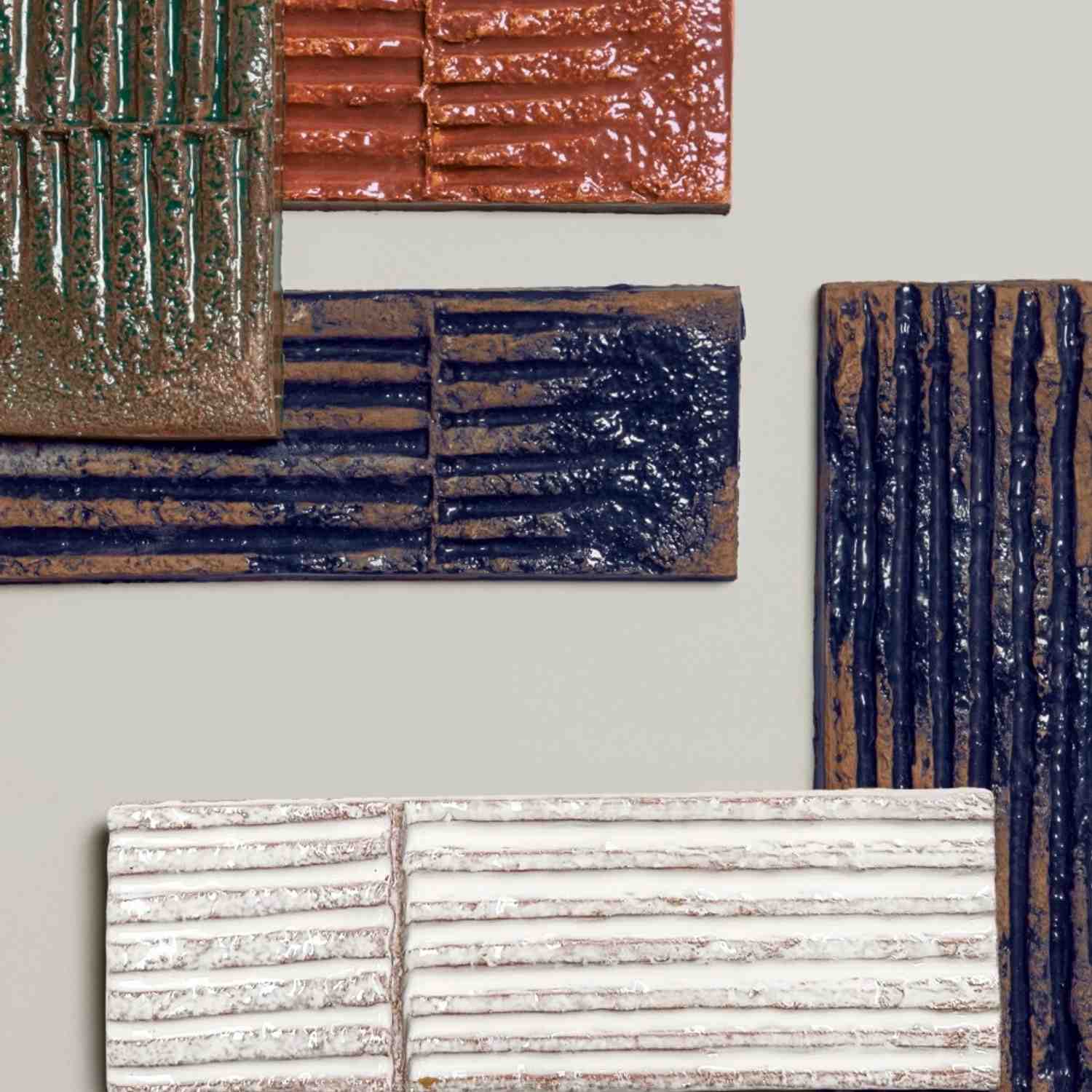 Mutina Chamotte high-gloss glazed ceramic wall tile samples displayed showing multiple colors and textures including Verde green Terra brown Nero dark blue and Ocra with pronounced tactile relief linear groove patterns