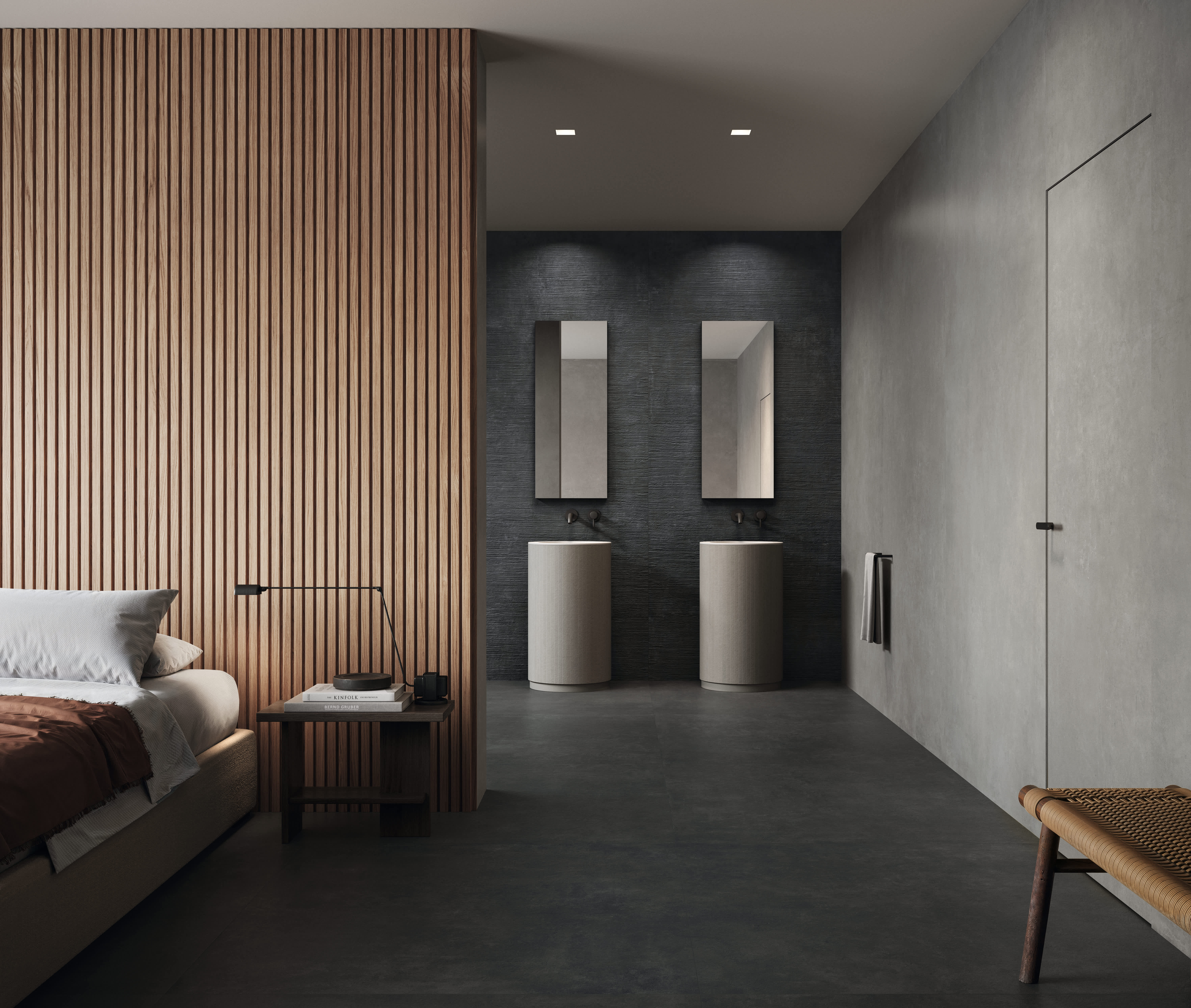 Concrete porcelain tile in a charcoal bedroom and ensuite, dark floor and walls beside a warm wood-slat partition, with twin pedestal basins and a low bed.