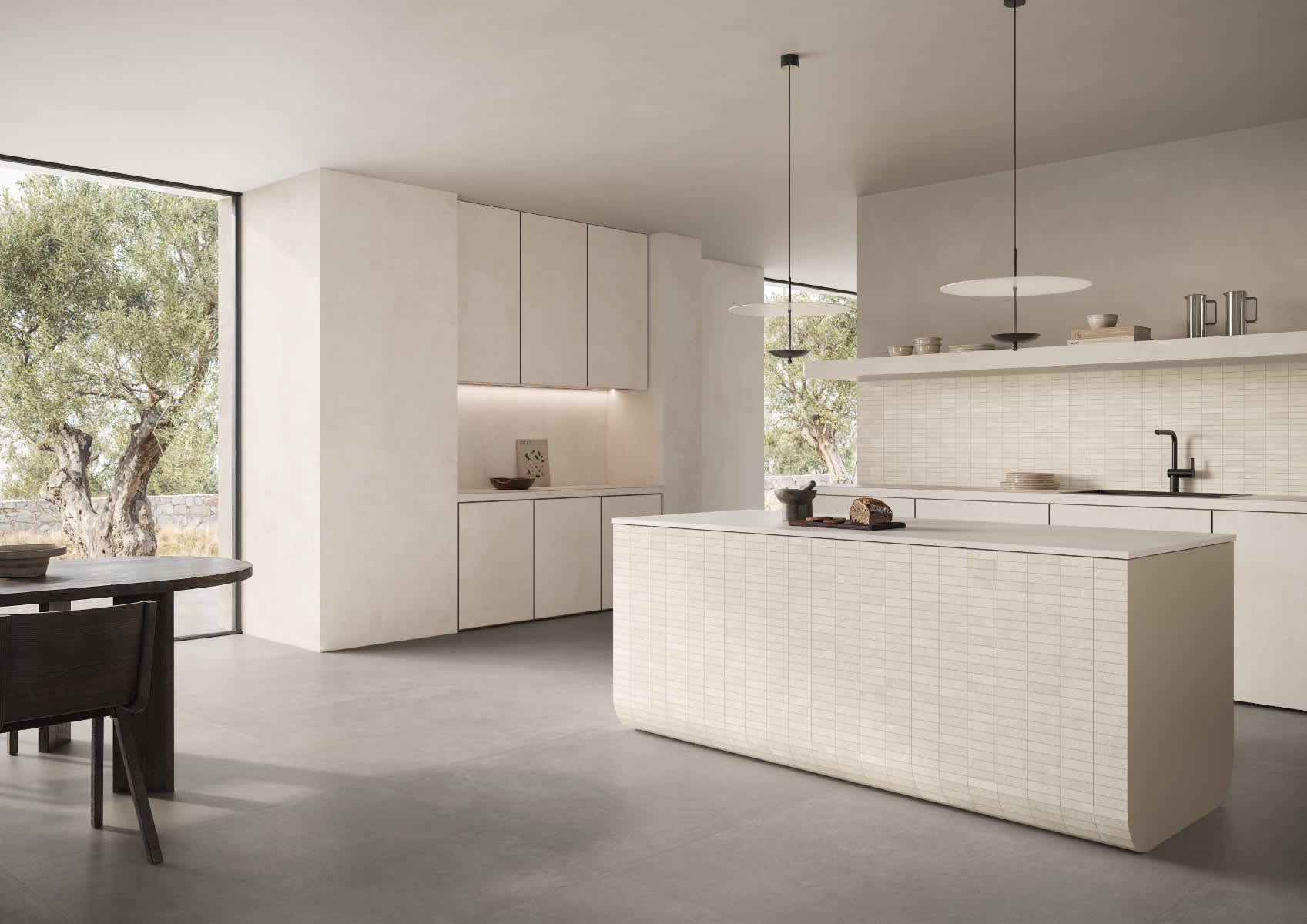 Impronta Concrete porcelain stoneware mosaic tiles in light white cream color with linear texture on kitchen backsplash and island front in modern kitchen with beige flat-panel cabinets white countertops pendant lights and large garden-view windows with o