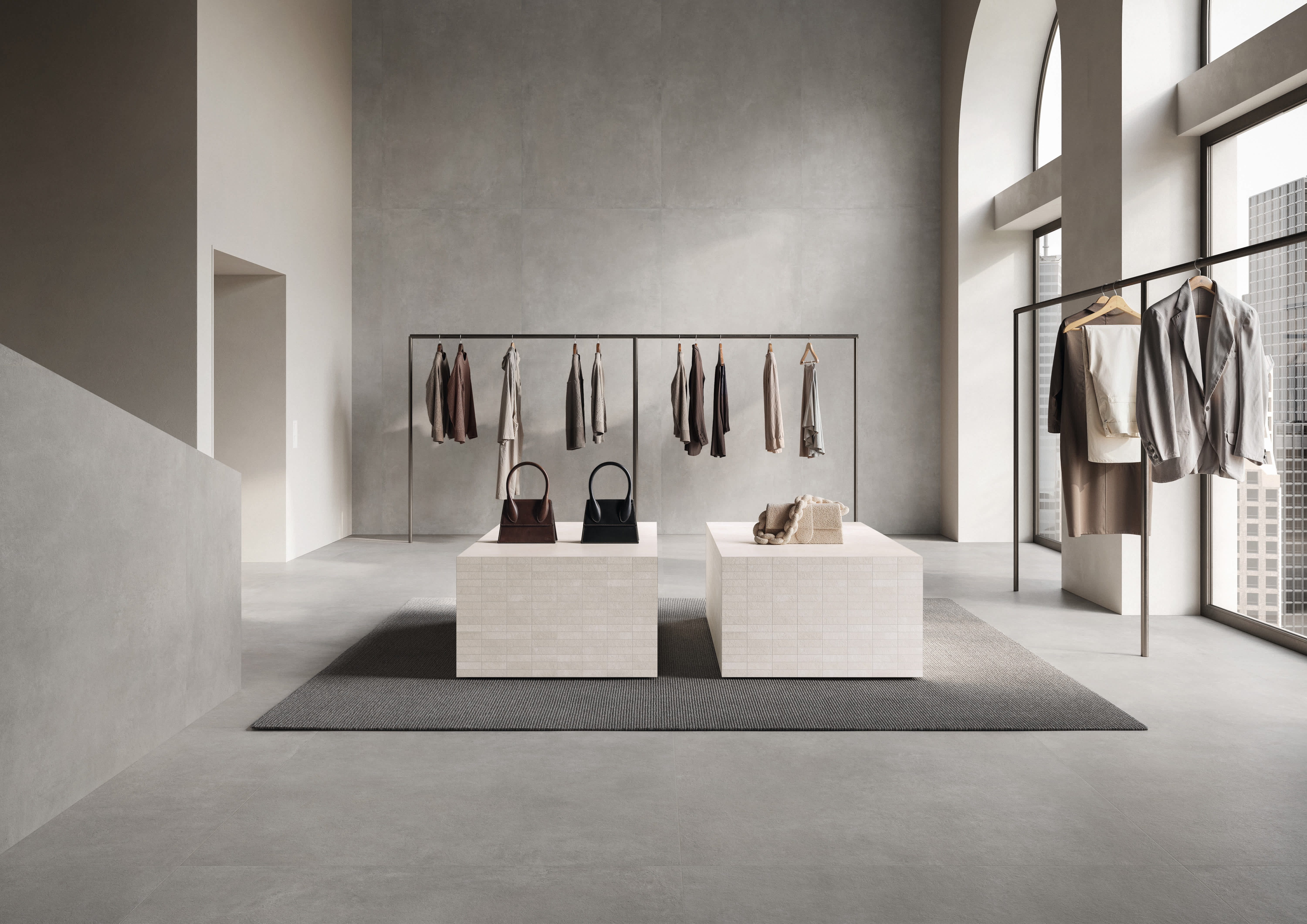 Concrete porcelain tile in a cool grey boutique, large-format walls and floor with clothing rails, display plinths and arched city-view windows.