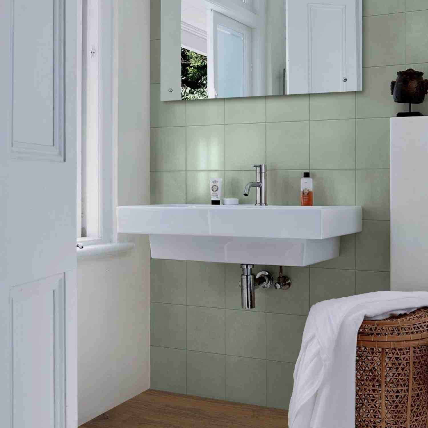Marazzi Contrasti glazed porcelain stoneware wall tiles in light sage green plain matte finish installed in bathroom with white wall-mounted sink chrome faucet rectangular mirror and bath products in bright natural light setting
