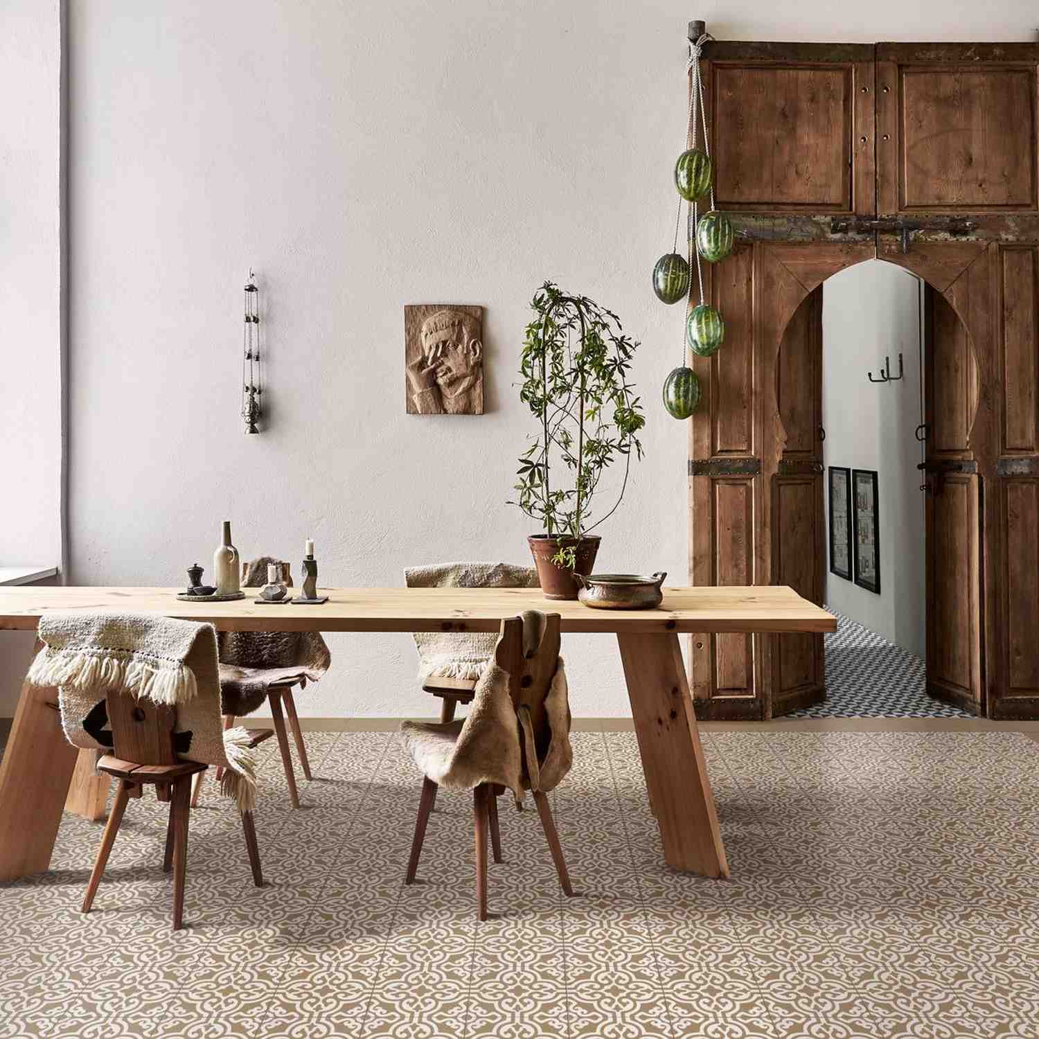 Marazzi Contrasti glazed porcelain stoneware decorative floor tiles in grey and white geometric Tappeto pattern in rustic bohemian dining room with large wooden armoire dining table wooden stools hanging green glass lanterns potted plants and carved wall