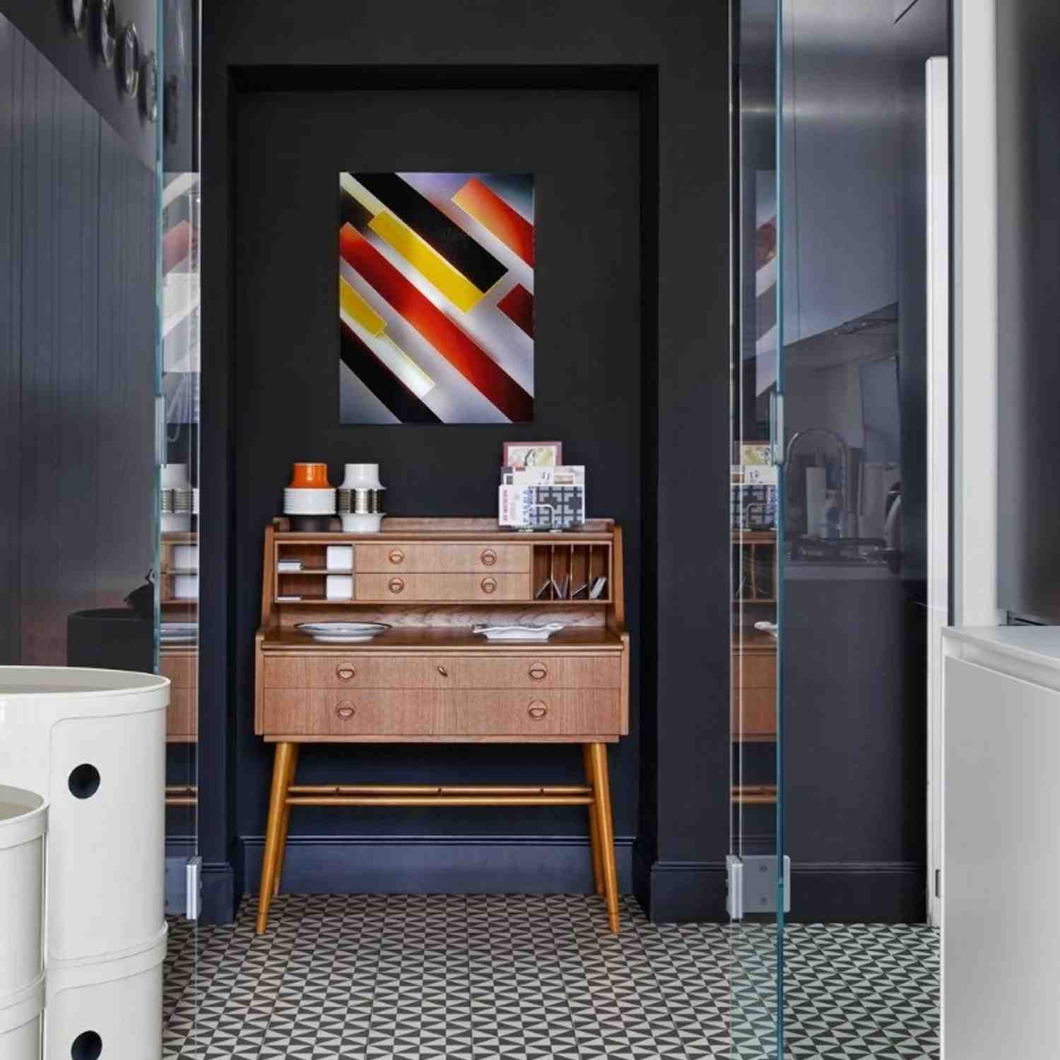 Marazzi Contrasti glazed porcelain stoneware wall tiles in dark charcoal black matte finish installed in moody entryway with colorful abstract geometric painting mid-century wooden console cabinet with drawers and contemporary decor accessories
