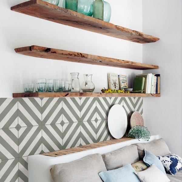 Marazzi Contrasti glazed porcelain stoneware decorative wall tiles in grey and white geometric diamond chevron Tappeto pattern with rustic wooden floating shelves displaying glass vases books and decorative objects above white sofa in living room
