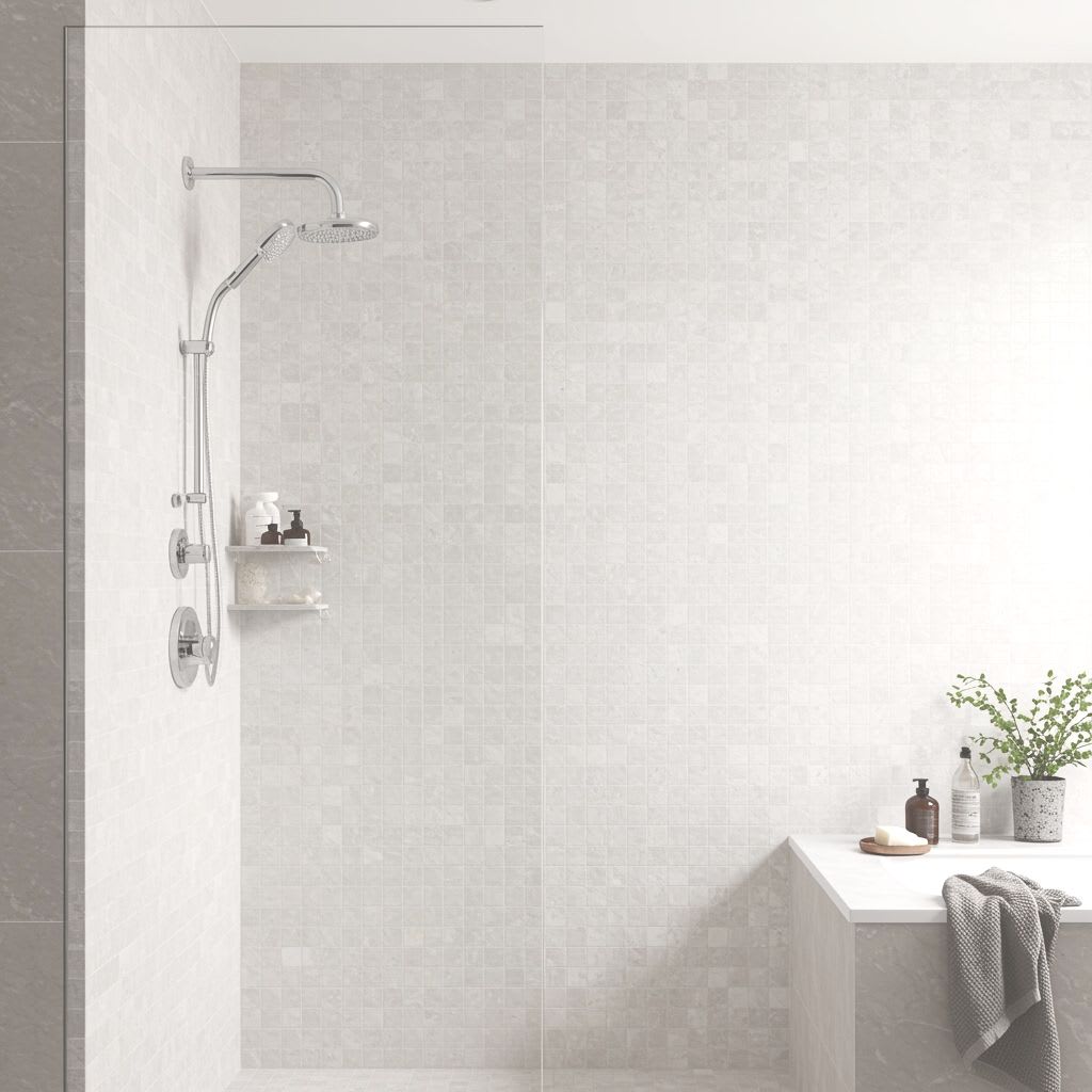 Pamesa Coralstone porcelain stoneware mosaic wall tiles in light beige cream coral stone finish installed in walk-in shower with chrome rain shower head handheld shower chrome controls wall-mounted white shelves with bath products potted green plant and d