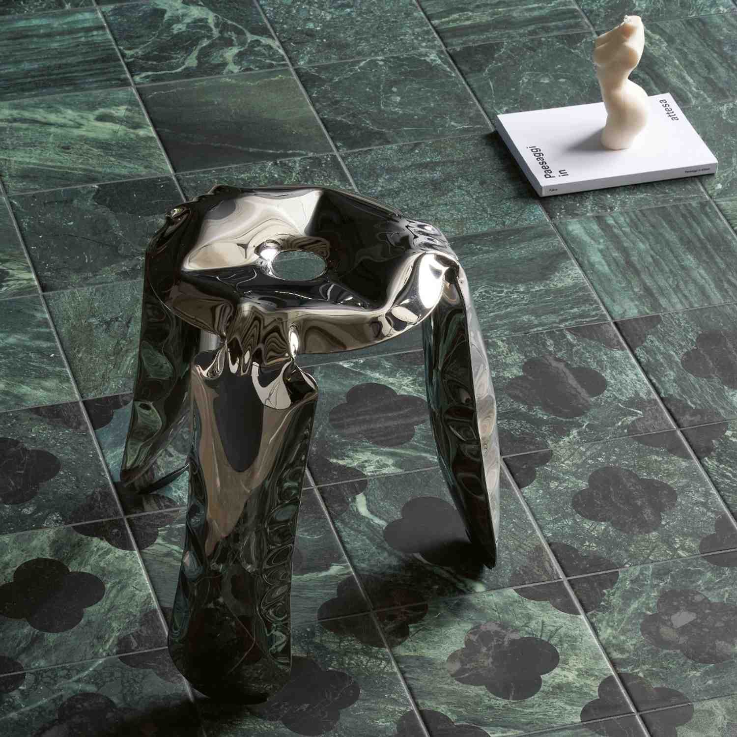 41zero42 Dandy glazed porcelain stoneware dark green marble-look floor tiles with white veining close-up detail with chrome metallic abstract sculptural object and white ceramic figurine on design magazine