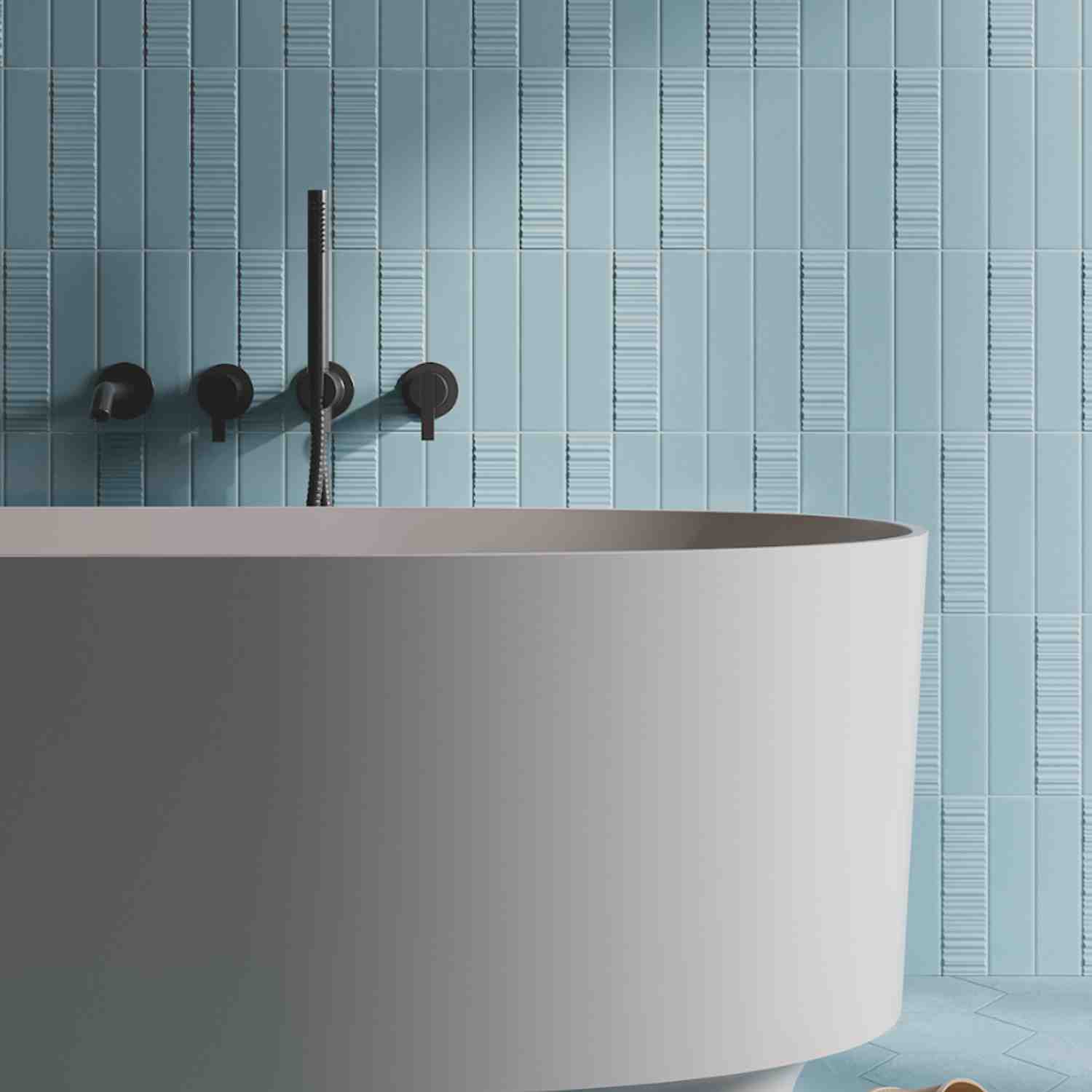 Elios Dust matte chevron ceramic wall tiles in ice light blue with vertical chevron pattern installed in modern bathroom with black wall-mounted faucet fixtures and white freestanding oval bathtub