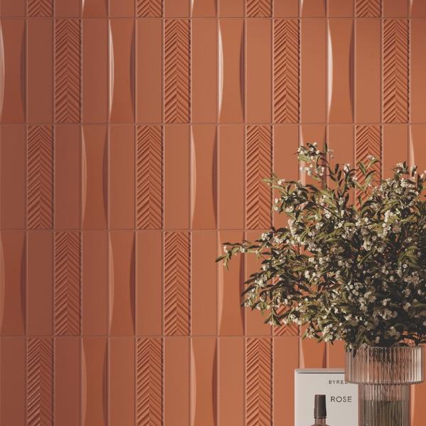 Elios Dust matte chevron ceramic wall tiles in dove warm terracotta with chevron pattern close-up showing textured surface with decorative green plant and luxury fragrance bottle on glass shelf