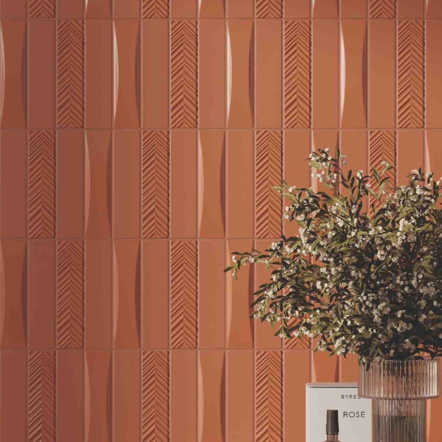 Elios Dust matte chevron ceramic wall tiles in dove warm terracotta with mixed chevron and wave relief pattern textures showing three-dimensional surface detail with flowering greenery in foreground