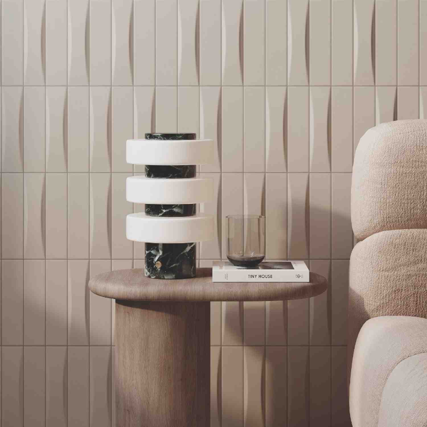 Elios Dust matte chevron ceramic wall tiles in dove light cream beige with wave relief pattern installed as living room accent wall with modern black and white marble stacked sculpture on round wooden side table book and cream boucle upholstered armchair