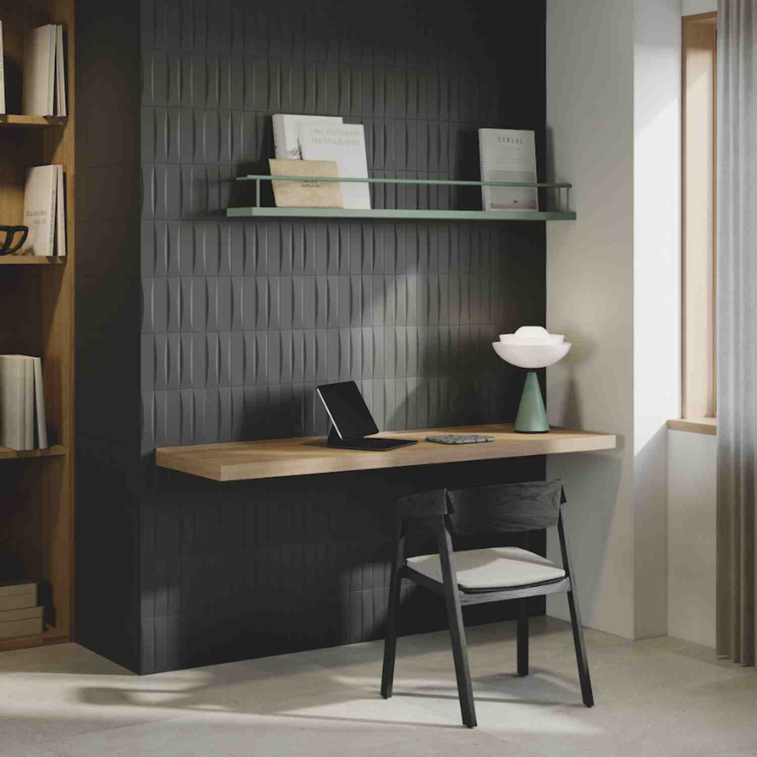 Elios Dust matte chevron ceramic wall tiles in ink dark charcoal installed as home office accent wall with floating wooden desk laptop green ceramic vase white lotus-shaped lamp and glass floating shelf with books and framed art