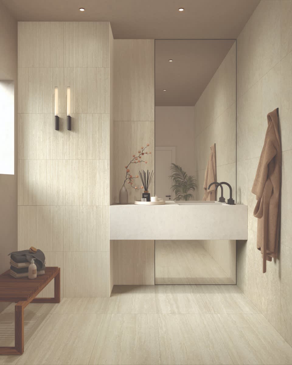 Castelvetro Firenze vein cut porcelain stoneware wall tiles in beige installed in modern bathroom with large format vertical layout black wall-mounted faucet fixtures modern linear wall sconces mirror cherry blossom branch decor brown towel and recessed c
