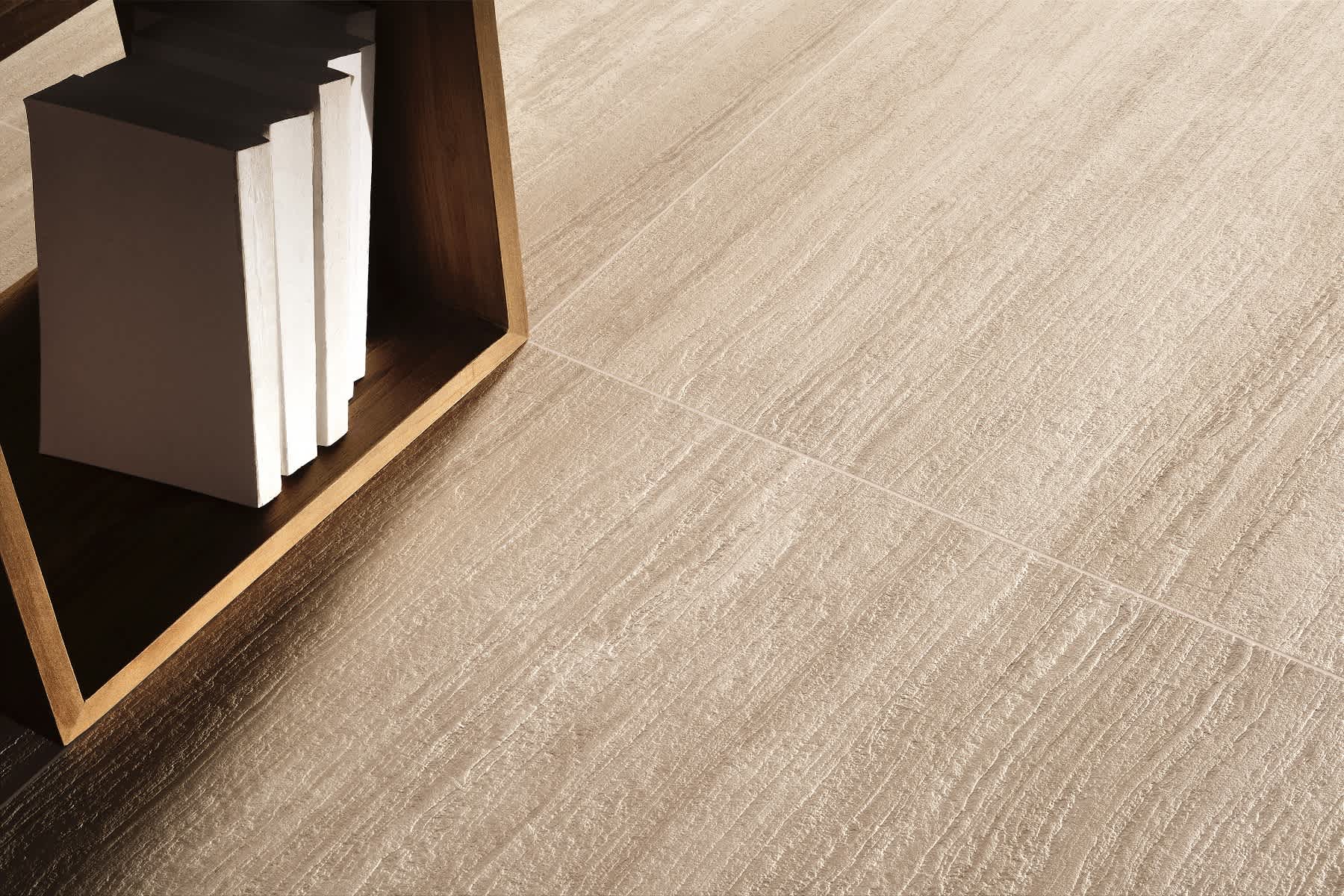 Coem Flow mosaic porcelain stoneware floor tiles in greige with linear wood grain texture installed in modern interior setting with dark wood bookshelf white books and warm natural lighting