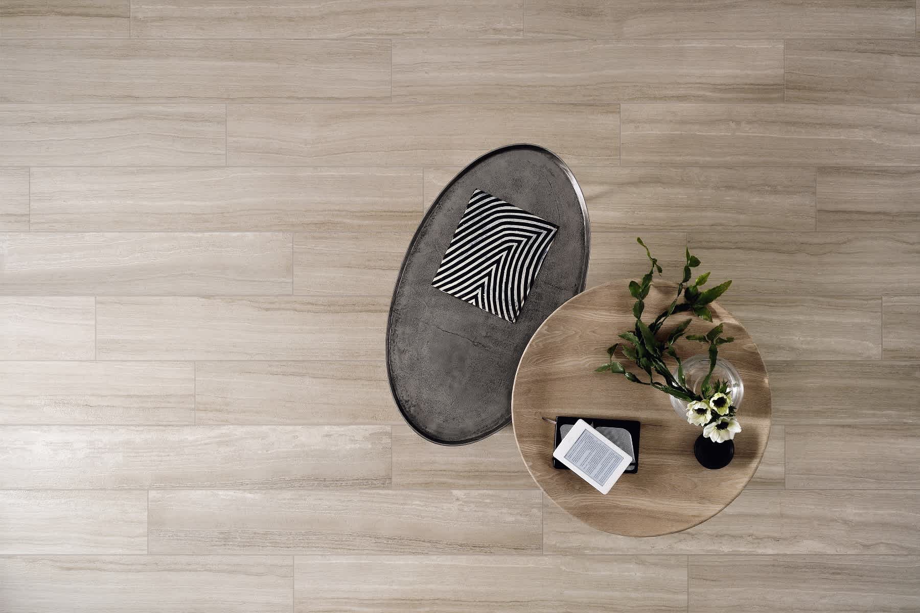 Coem Flow mosaic porcelain stoneware floor tiles in light greige wood grain finish shown from above with round wooden coffee table dark metal oval side table striped decorative tray open book and glass vase with fresh flowers