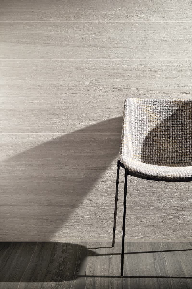 Coem Flow mosaic porcelain stoneware wall tiles in ivory white with horizontal brushed striation texture installed in minimalist interior with houndstooth upholstered chair and natural shadow play