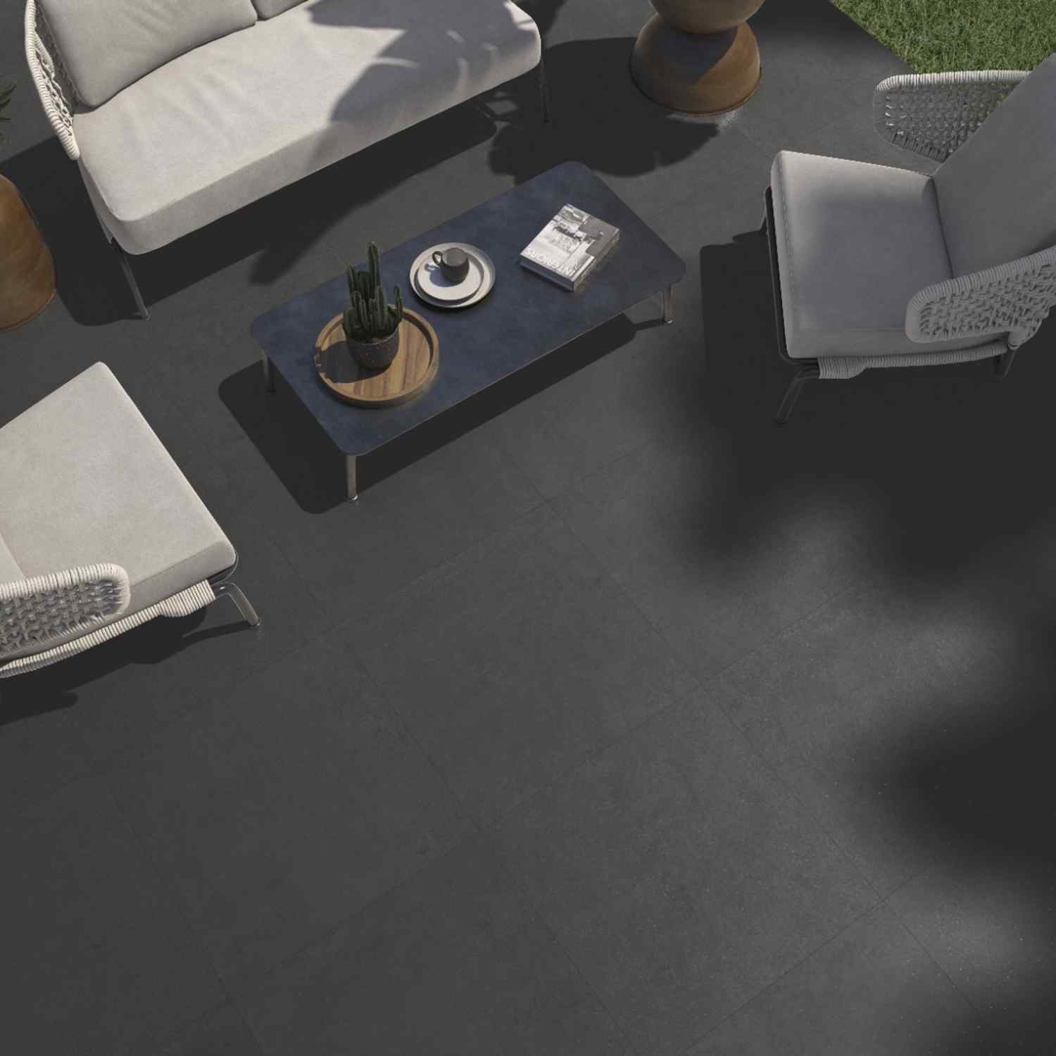 Argenta Gravel porcelain stoneware outdoor floor tiles in shadow dark grey with matte stone-cement finish on patio terrace with white cushioned lounge furniture dark coffee table and garden setting top-down view