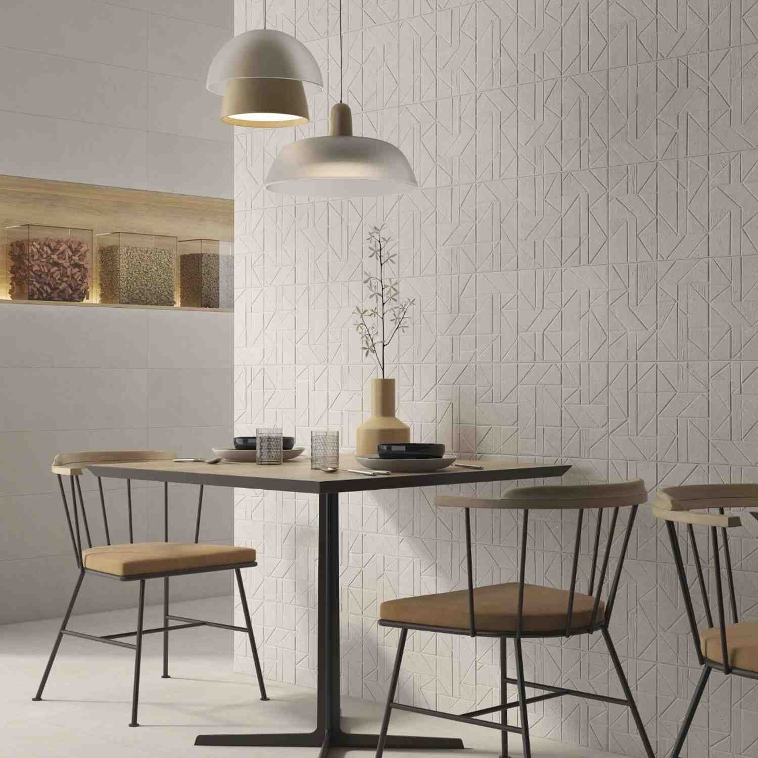 Argenta Gravel porcelain stoneware wall tiles in cream white with geometric chevron textured relief pattern in dining area featuring white dome pendant lights wooden dining table ceramic vases decorative plant and pantry shelving with glass storage jars