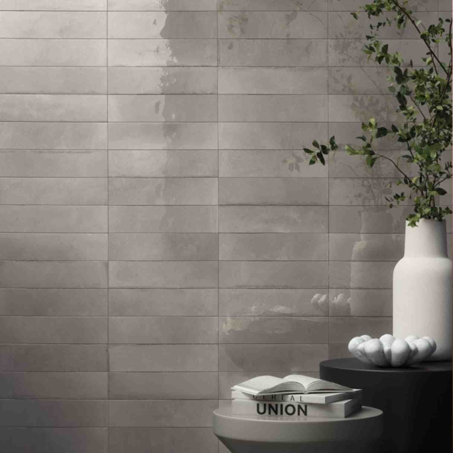 Refin Halo porcelain wall tiles in basil gloss lustre finish with warm grey-green tone featuring 6x24 format brick-lay pattern with white ceramic vase trailing greenery and natural light highlighting the glossy surface