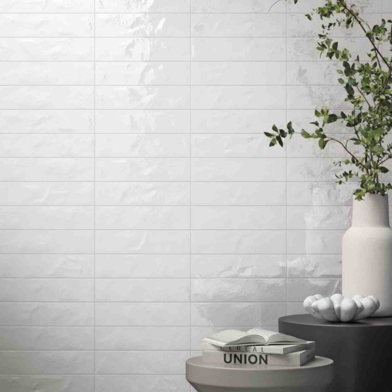 Refin Halo porcelain wall tiles in cotton gloss lustre finish with soft white tone featuring 6x24 format brick-lay pattern with white ceramic vase trailing greenery and clean luminous surface reflecting natural light