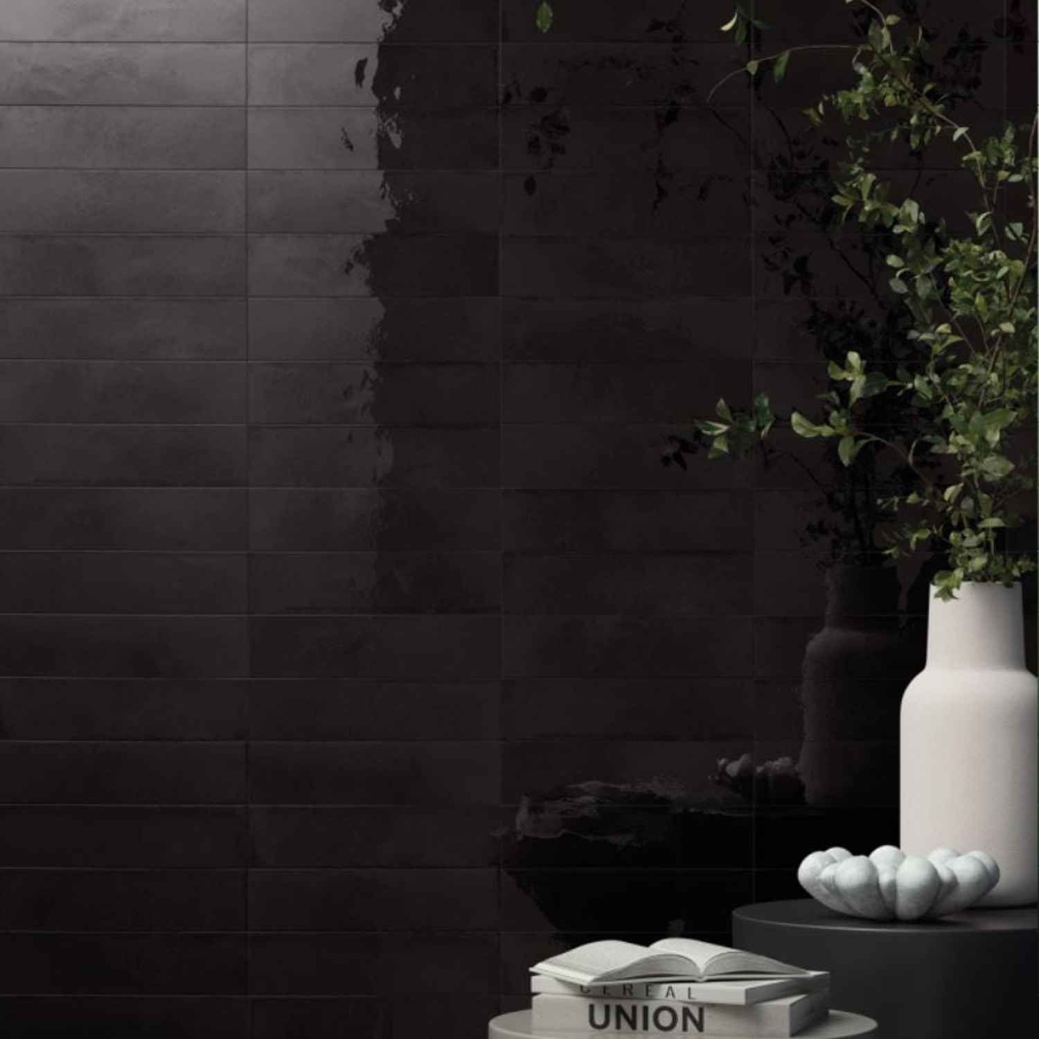 Refin Halo porcelain wall tiles in chrome gloss lustre finish with dark charcoal black tone featuring 6x24 format brick-lay pattern with white ceramic vase trailing greenery and dramatic deep reflective surface