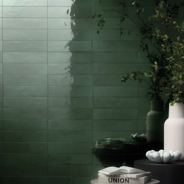 Refin Halo porcelain wall tiles thumbnail in ocean gloss lustre finish with deep green tone showing 6x24 brick-lay pattern styled with white vase trailing greenery stacked books and decorative objects
