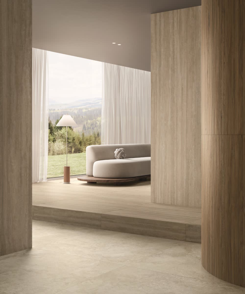 Caesar Iconica mosaic porcelain tile in warm beige Navona Verso wood-grain finish as wall cladding in modern living room with white curved sofa floor lamp sheer curtains and mountain landscape view