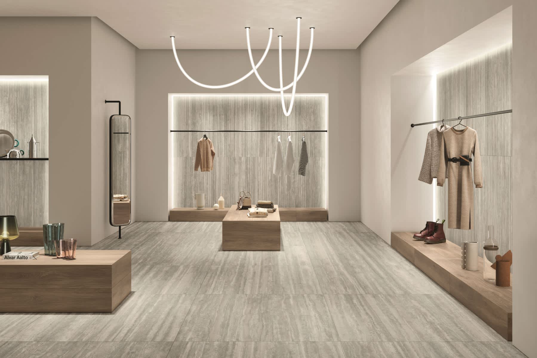 Caesar Iconica mosaic porcelain tile in warm beige and silver grey tones as wall cladding and flooring in luxury retail boutique with backlit display walls clothing racks sculptural white LED ceiling light wooden benches and full-length mirror