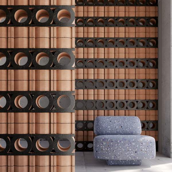 Mutina Jali 3D terracotta screen wall installation in interior setting with natural terracotta and nero blocks creating decorative partition with grey textured armchair in foreground