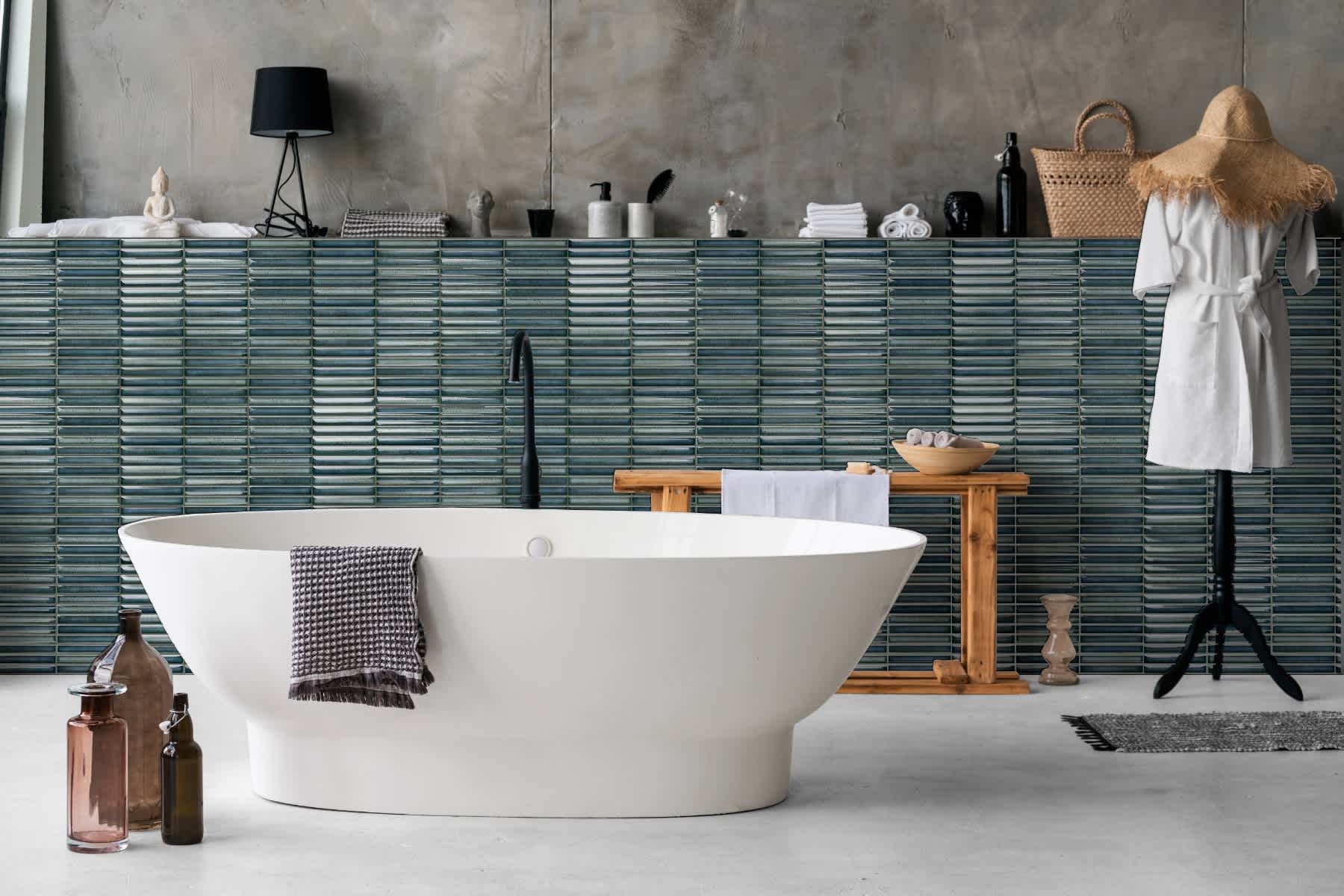 Estudio Ceramico Karatsu glazed porcelain wall tiles in teal green horizontal linear pattern installed in luxury bathroom with freestanding white bathtub black fixtures and wooden bench accessories