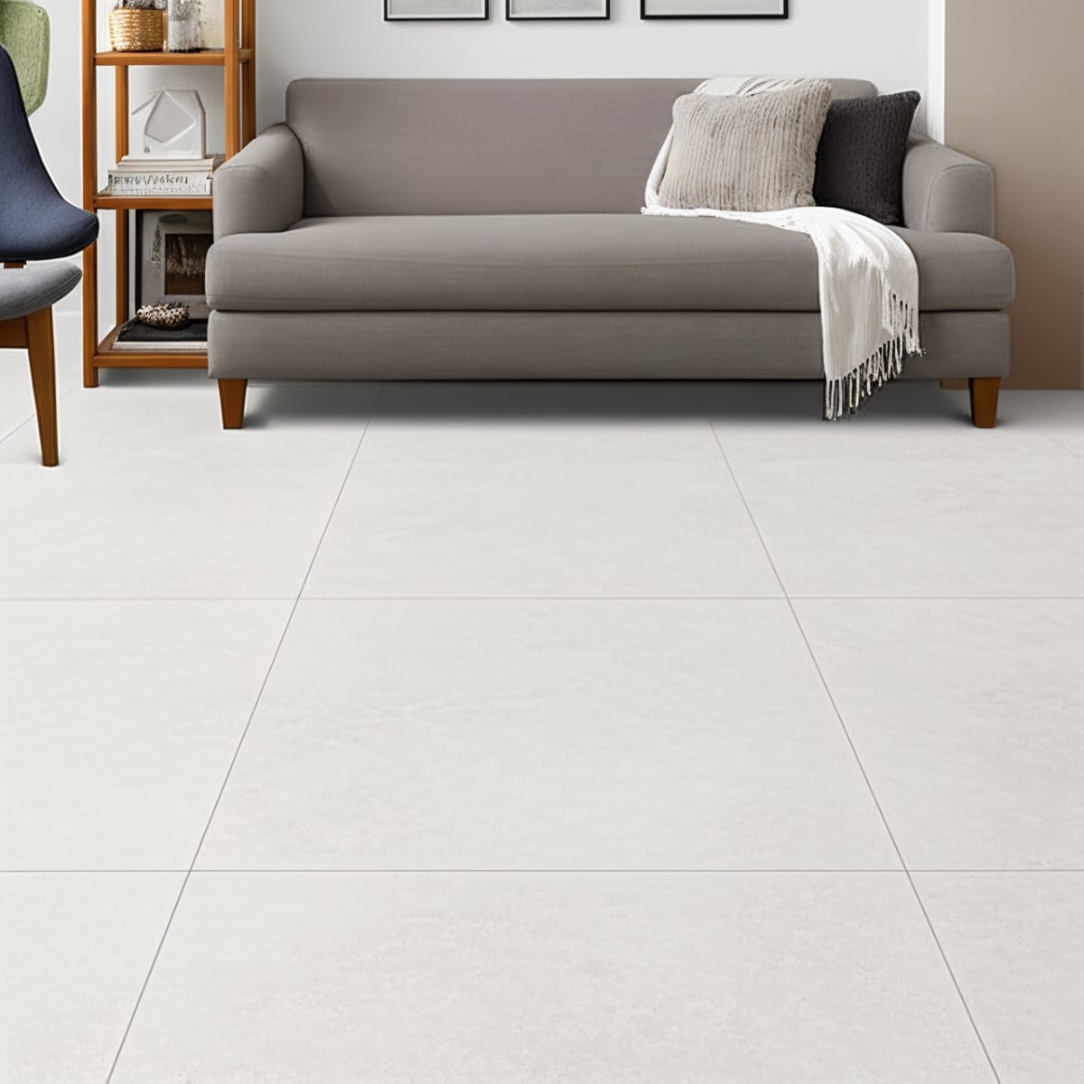 Overland Limestone ivory matte porcelain floor tiles close-up in living room setting with grey sofa, fringed throw blanket, wooden side shelf, and subtle limestone veining detail