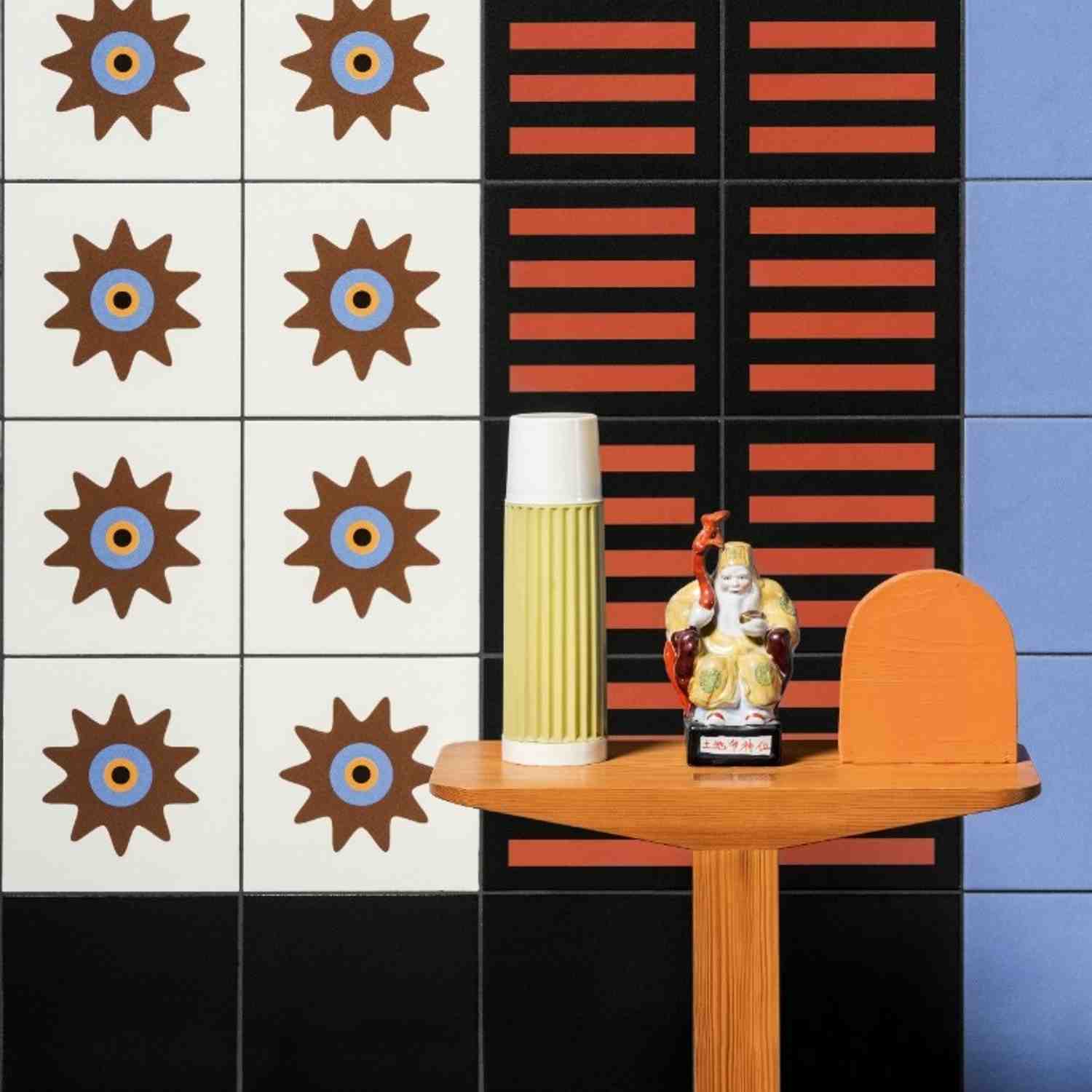 Mutina Margherita starburst sun graphic pattern tiles in brown and blue on white alongside black tiles with red horizontal stripes, styled with decorative ceramic vase and figurine