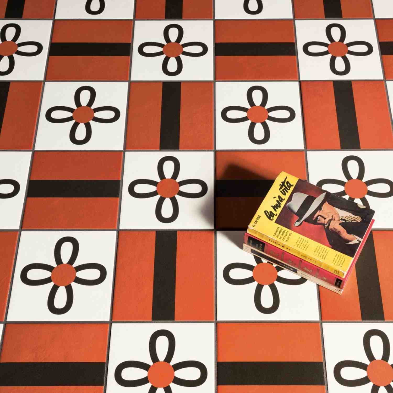 Mutina Margherita terracotta, black, and white Petals flower graphic pattern porcelain floor tiles in checkerboard layout with vintage book as decorative styling
