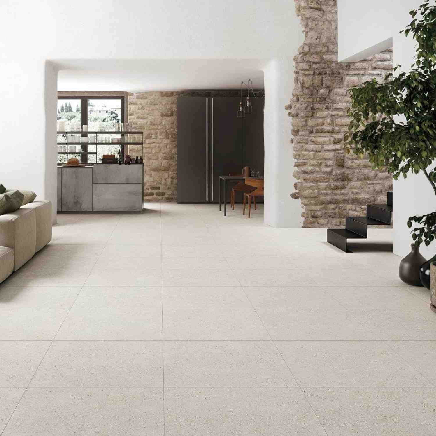Refin Masterplan open-plan living space with large format Mist porcelain floor tiles, exposed stone accent walls, industrial black metal shelving, dining area and indoor tree