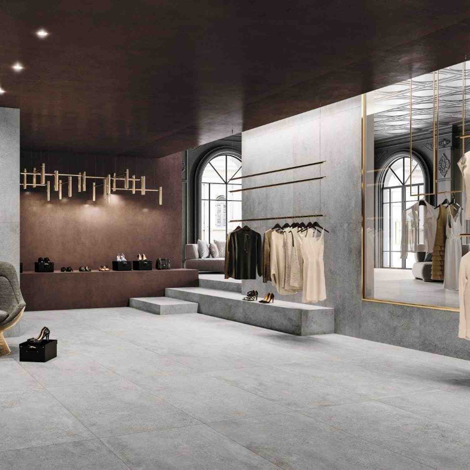 Refin Masterplan luxury retail boutique with grey Mist porcelain floor tiles and steps, Cinder accent wall, arched windows with gold trim, clothing display racks, modern chandelier
