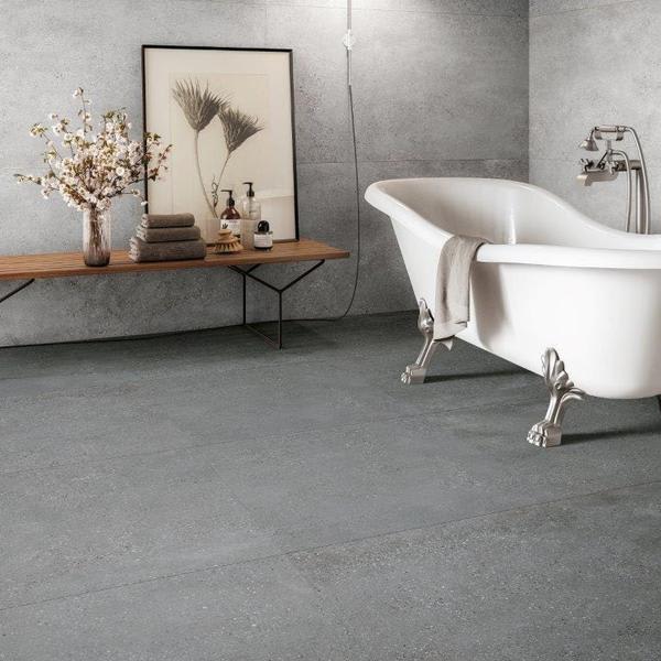 Refin Masterplan bathroom with clawfoot bathtub on dark grey porcelain floor tiles, wooden bench with framed art and dried flowers, concrete-look wall tiles