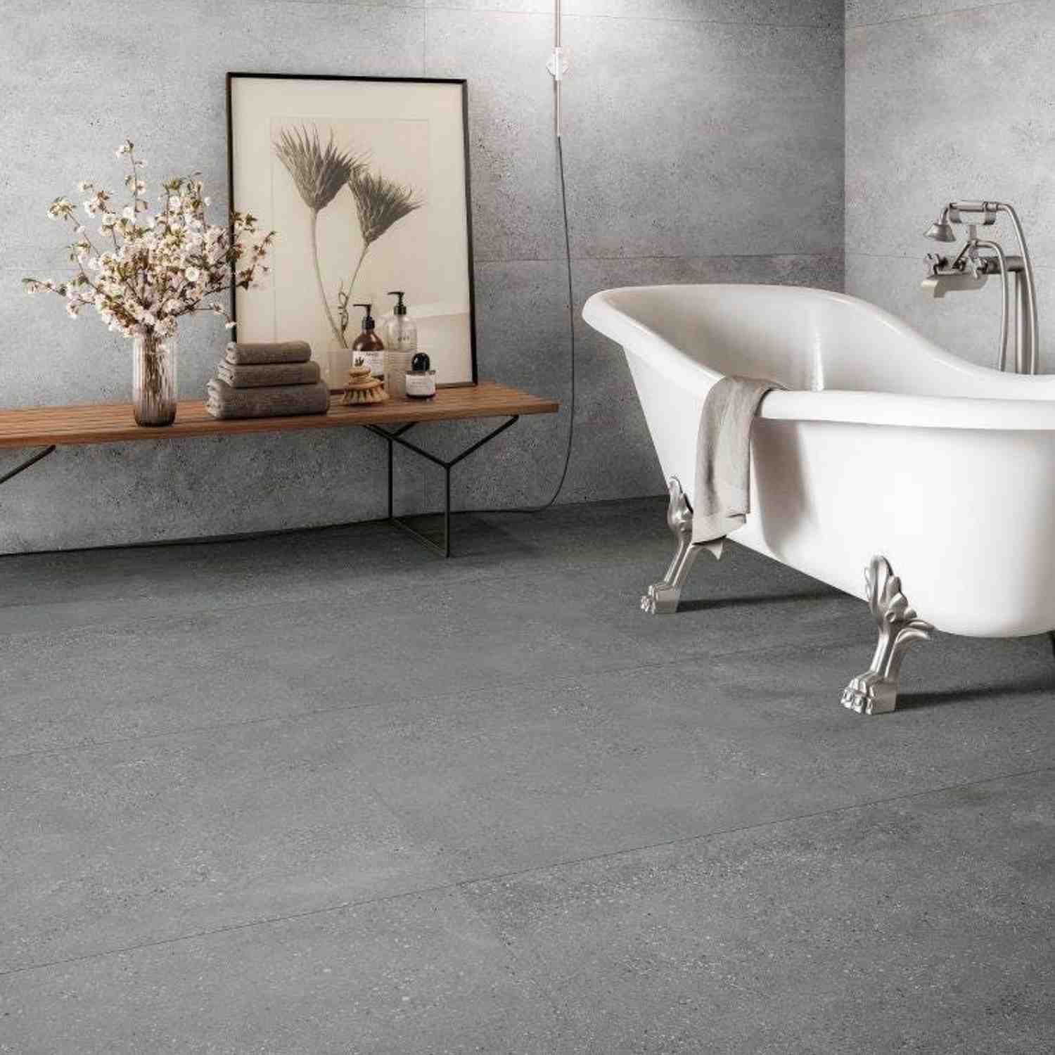 Refin Masterplan porcelain stoneware bathroom with classic clawfoot bathtub on dark grey Mist floor tiles, wooden bench with framed art and dried flowers, concrete-look grey wall tiles