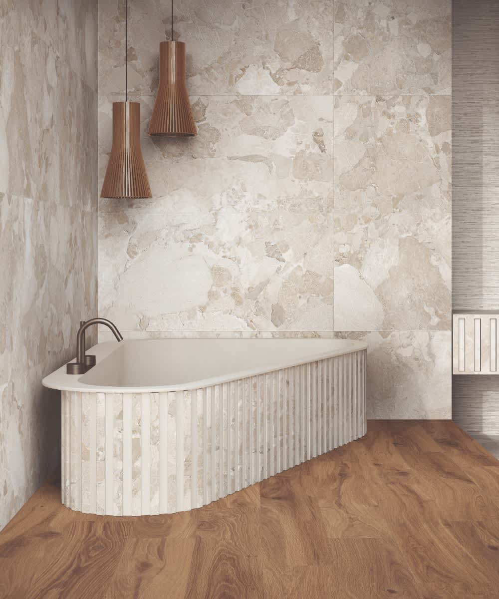 Ergon Materastone Sassi Beige porcelain stoneware wall tiles in an elegant bathroom with freestanding bathtub, wooden slatted pendant lights, and bronze wall-mounted faucet