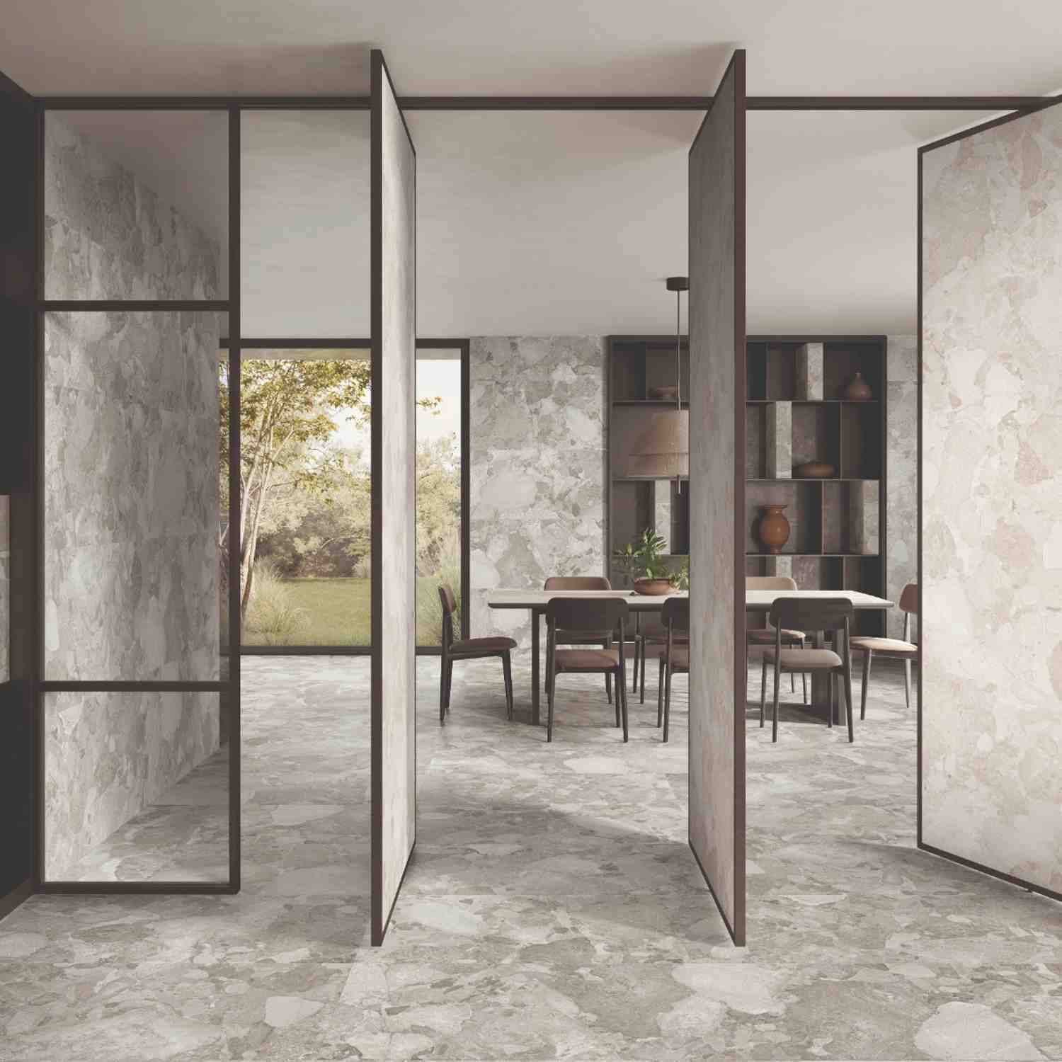 Ergon Materastone Sassi Greige porcelain stoneware wall and floor tiles in a contemporary dining room with glass partition doors, wooden dining table, upholstered chairs, built-in shelving, and garden views