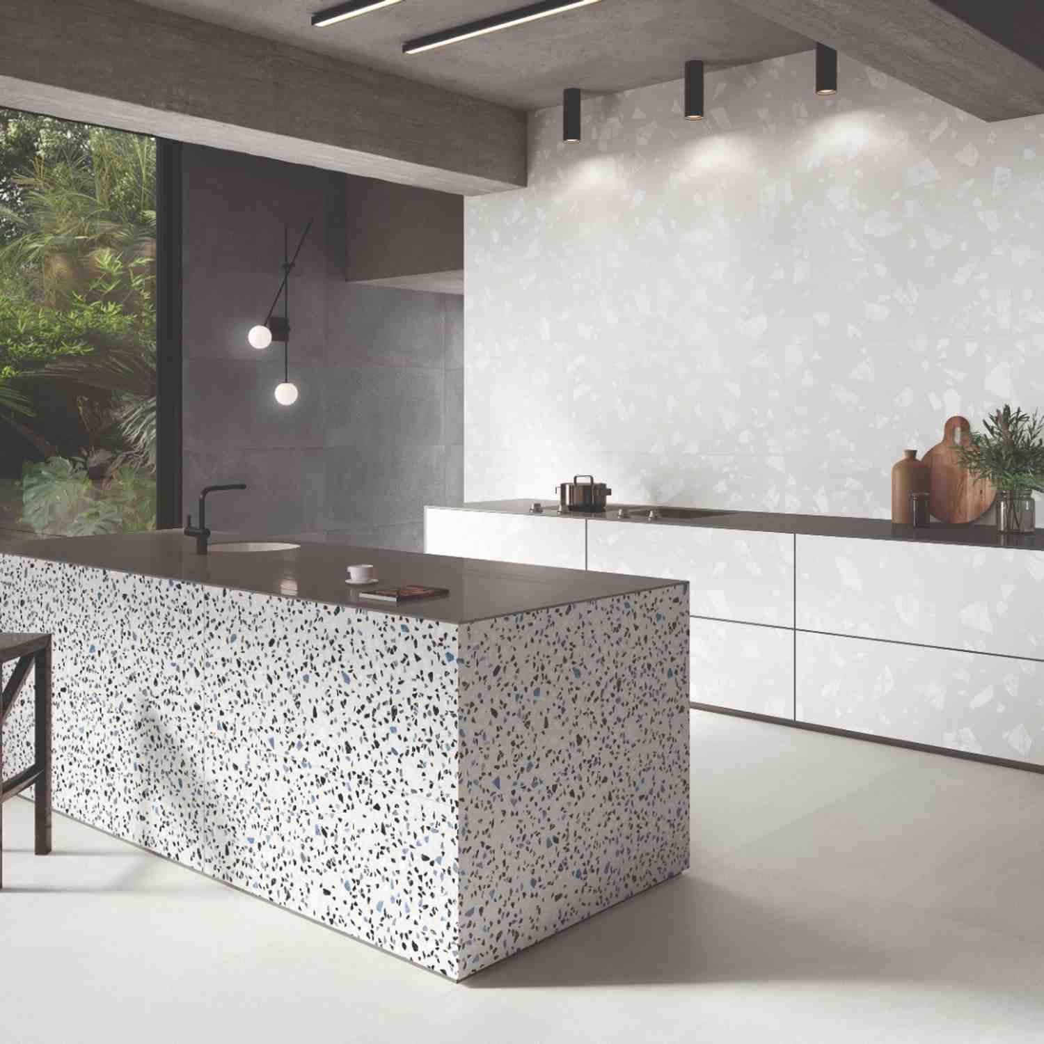 Emilceramica Medley Grey Minimal matte porcelain wall tiles with White Minimal Pop terrazzo-style kitchen island in a modern kitchen with dark countertops, globe pendant light, black fixtures, and tropical garden view