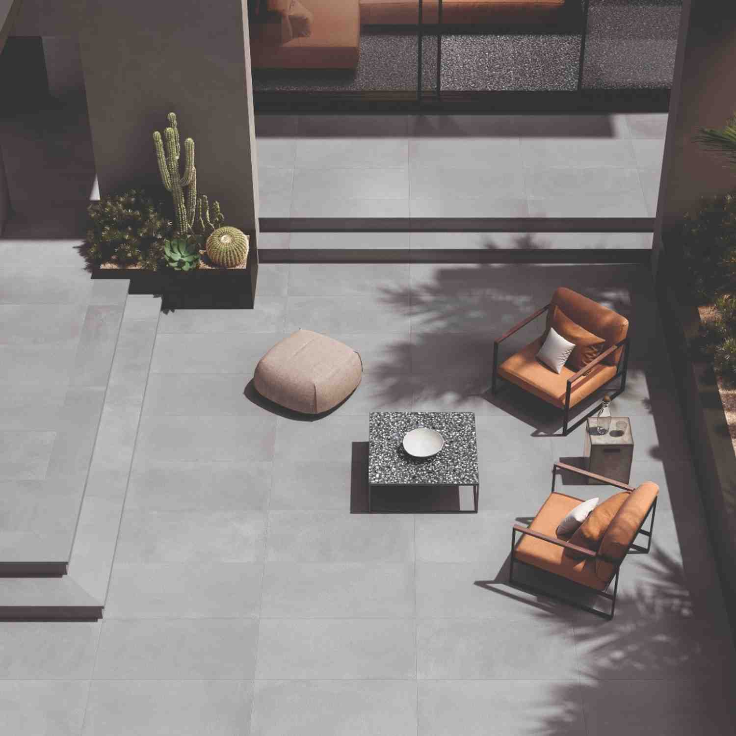 Emilceramica Medley Dark Grey Minimal matte porcelain outdoor patio tiles seen from above with leather lounge chairs, fabric pouf, cacti planter, and terrazzo-style Pop accent table