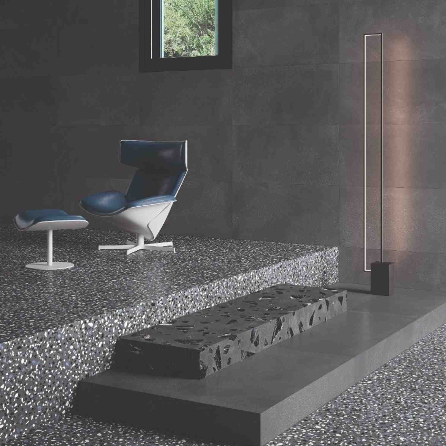 Emilceramica Medley Dark Grey Minimal matte porcelain wall tiles with Pop Dark Grey terrazzo-style floor tiles in a modern living space with blue mid-century lounge chair, slim LED floor lamp, and garden view