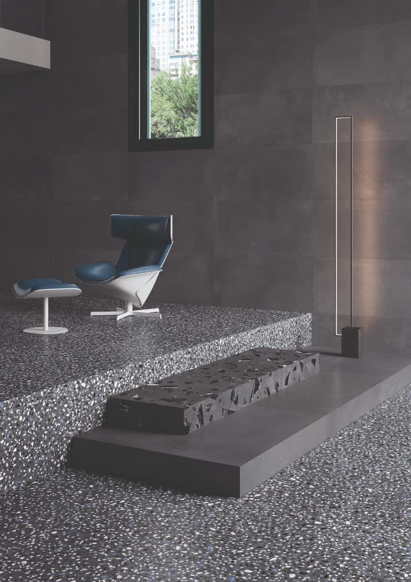 Emilceramica Medley Dark Grey Minimal walls with Pop Dark Grey terrazzo mosaic floor tiles in a modern living space with blue mid-century lounge chair, slim LED floor lamp, and garden window view