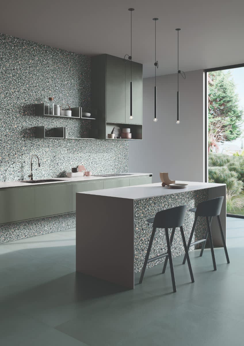 Emilceramica Medley Green Minimal Pop terrazzo mosaic wall tiles in a modern kitchen with dark green cabinetry, open shelving, pendant lights, white countertop island with bar stools, and garden window