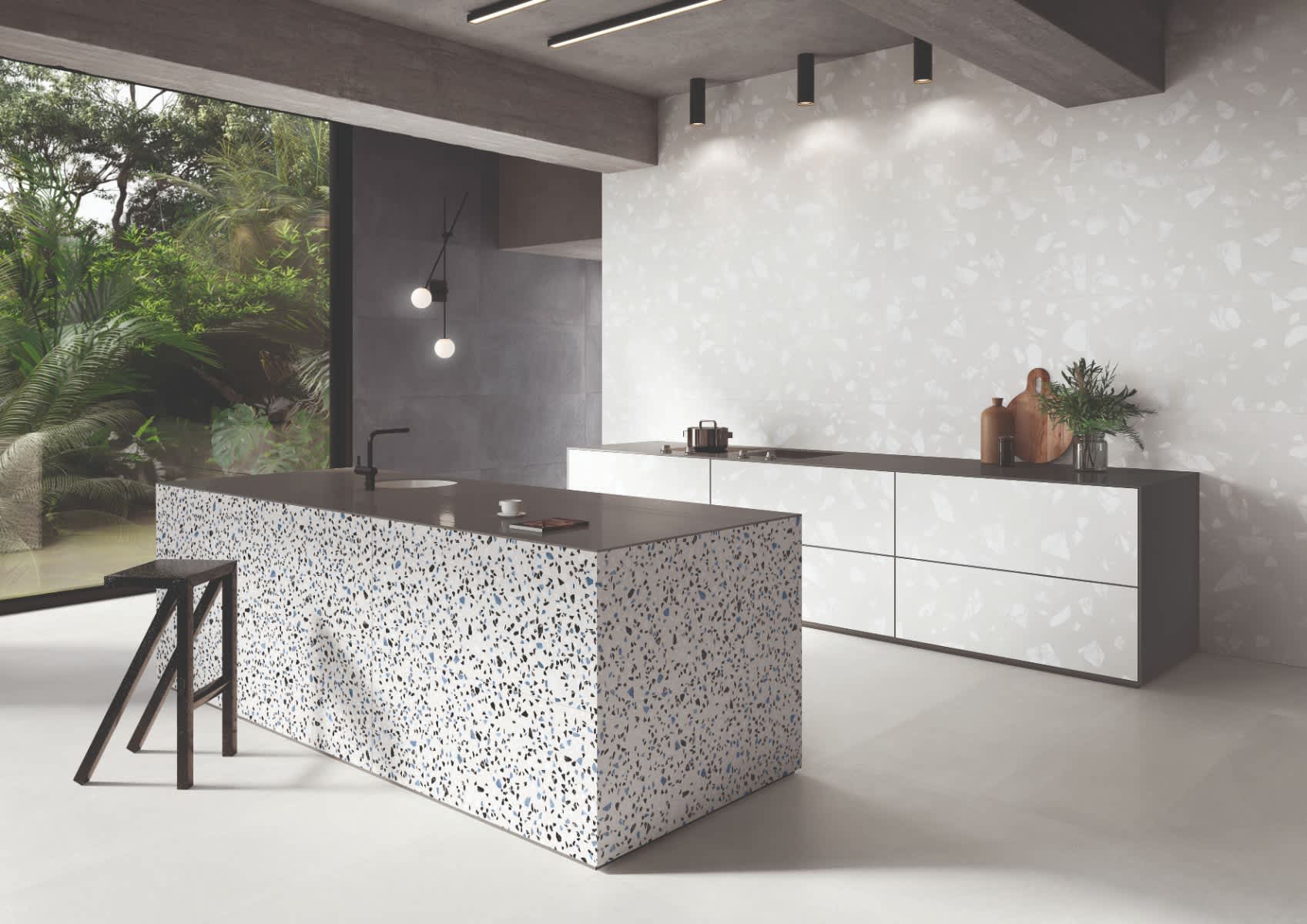 Emilceramica Medley Grey Minimal walls with White Minimal Pop terrazzo mosaic kitchen island front, dark countertops, globe pendant light, black fixtures, bar stools, and tropical garden view